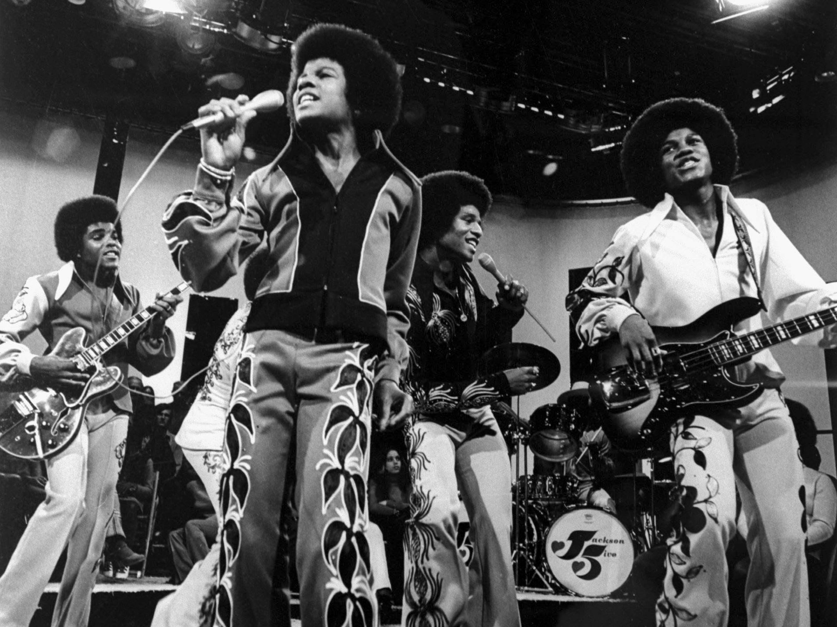 Jackson Five in 1972 in Los Angeles, California in a black-and-white shot. They wear fun pants, play lots of instruments, and have impressive afros.