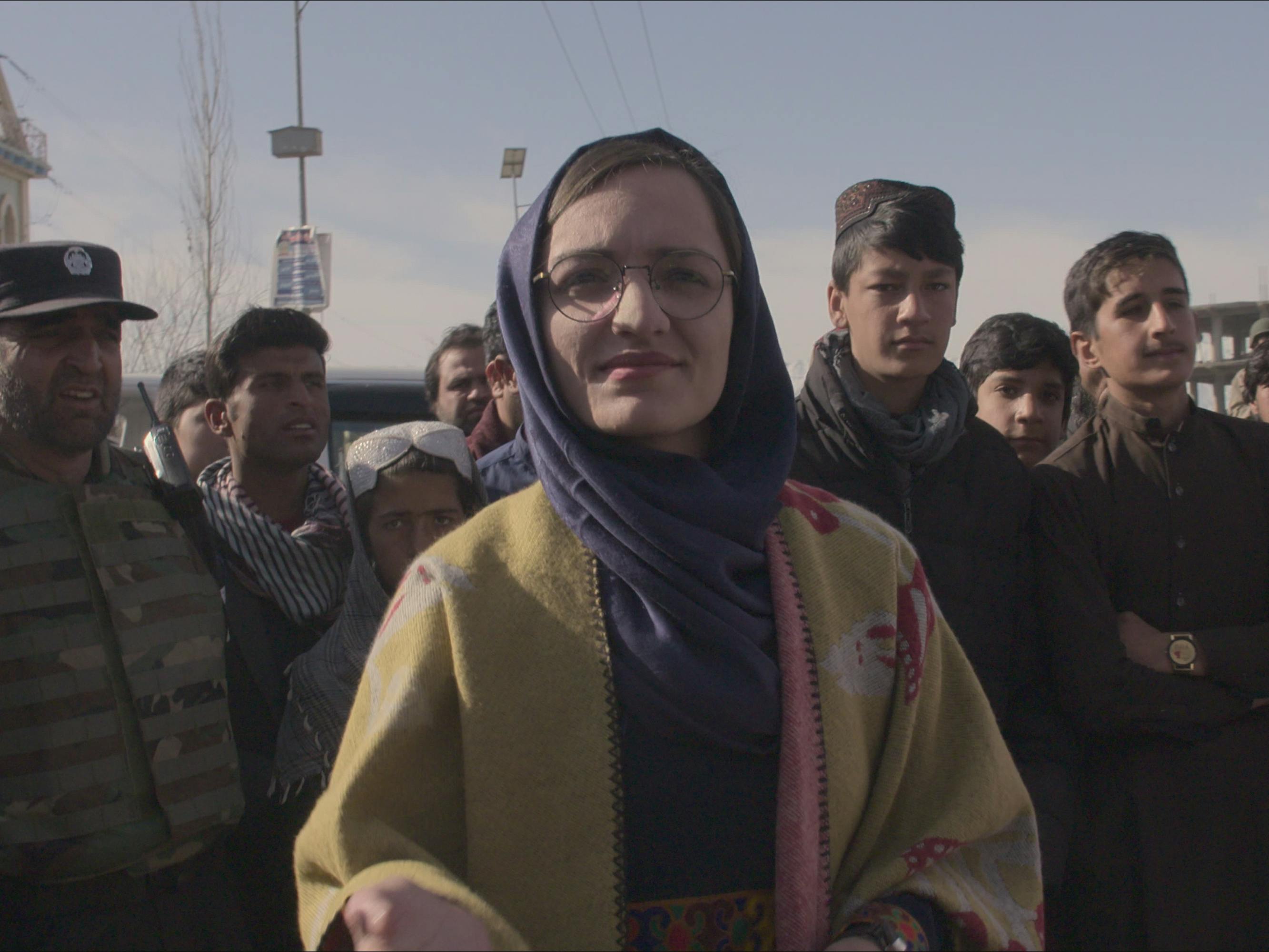 A crowd from In Her Hands stands in the sun against a blue sky.