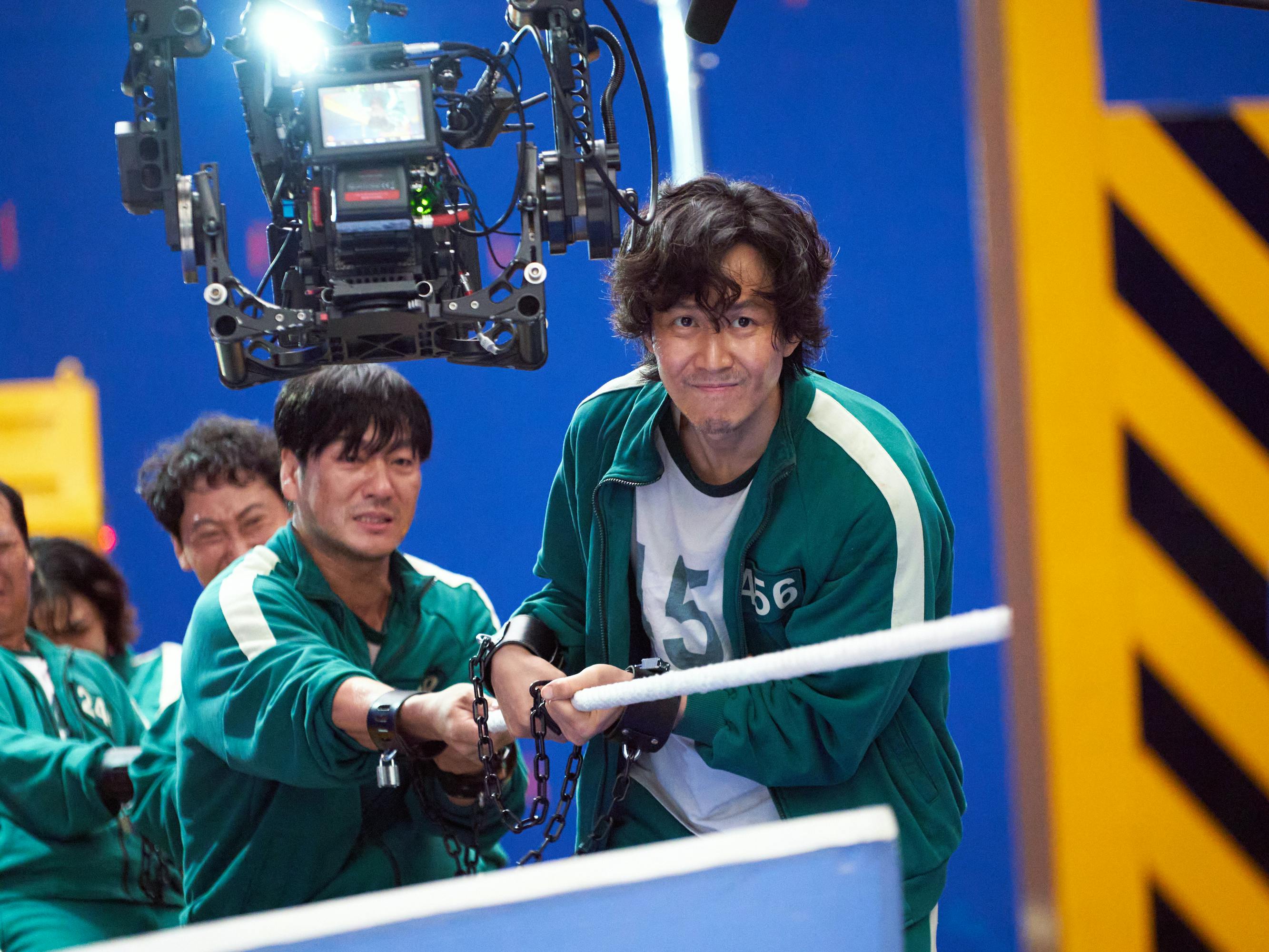 Cho Sang-woo (Park Hae-soo) and Seong Gi-hun (Lee Jung-jae) play tug of war with other teammates.