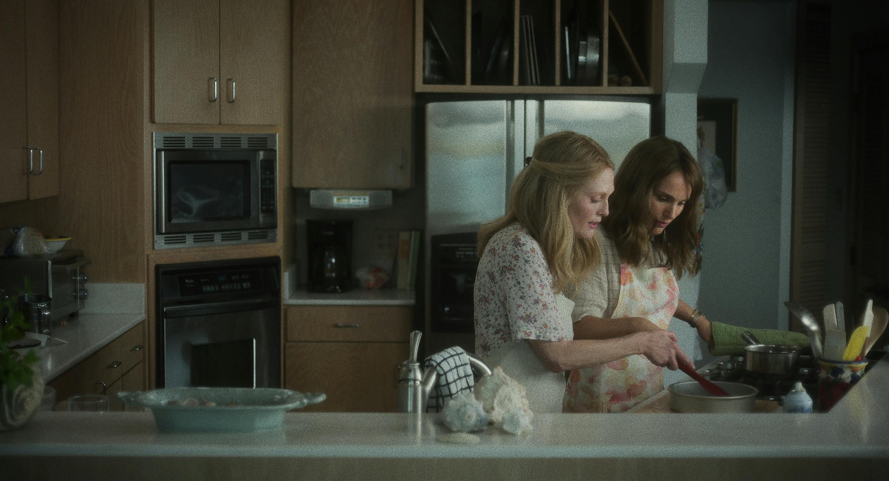 Gracie Atherton-Yoo (Julianne Moore) shows Elizabeth Berry (Natalie Portman) how to bake a cake. Both women wear floral and aprons.