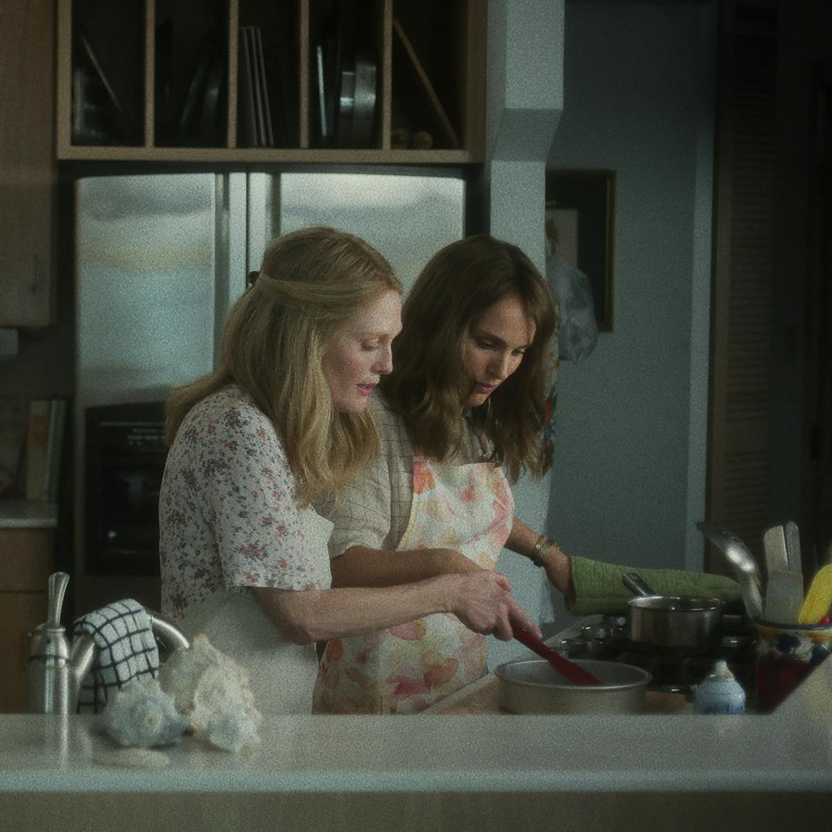 Gracie Atherton-Yoo (Julianne Moore) shows Elizabeth Berry (Natalie Portman) how to bake a cake. Both women wear floral and aprons.