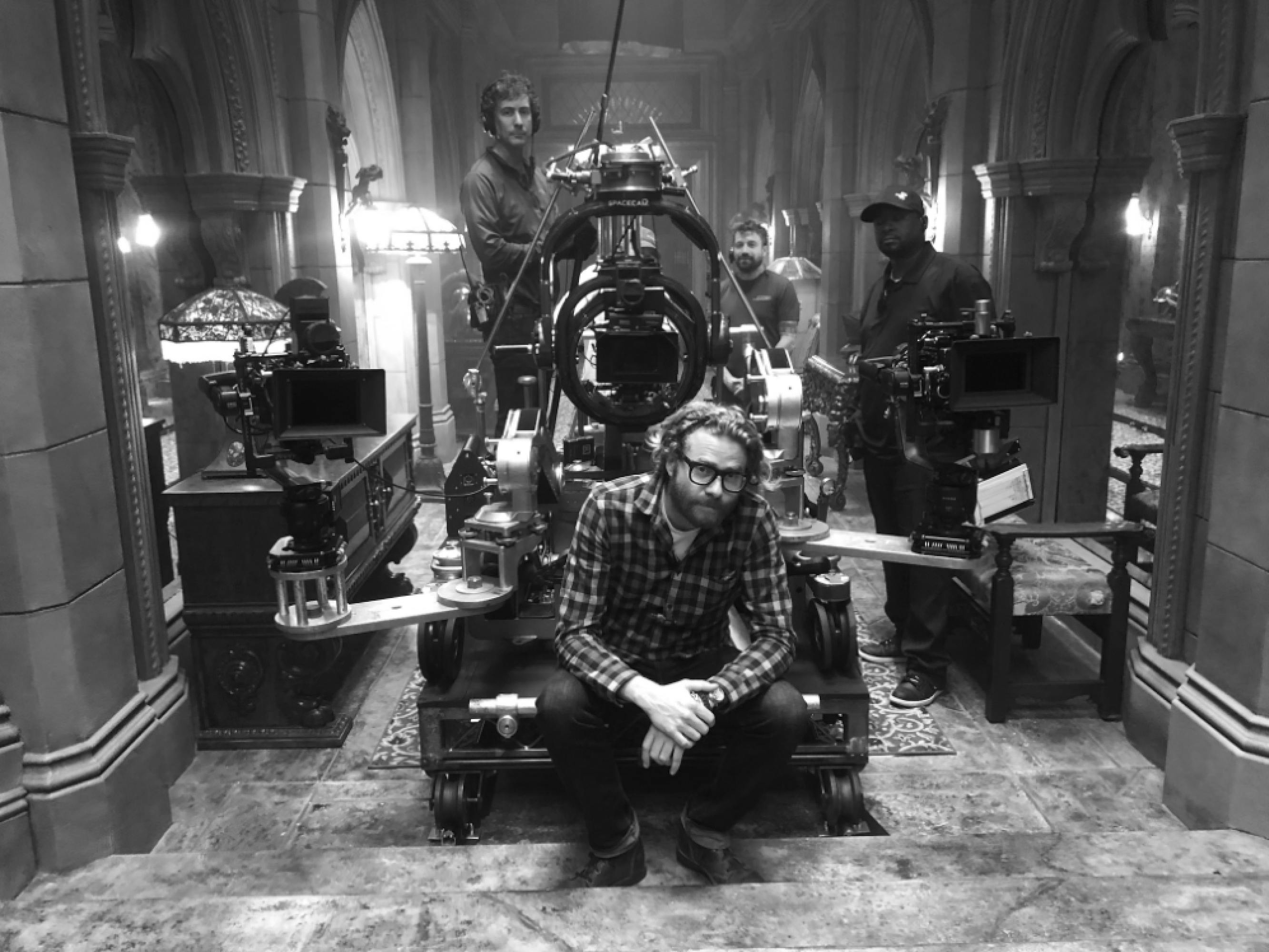 Cinematographer Erik Messerschmidt sits on a camera rig which is positioned in a hallway at the Hearst Castle replicated set of Mank. Some of the crew are behind the rig, operating cameras as Messerschmidt takes a moment to pause. 