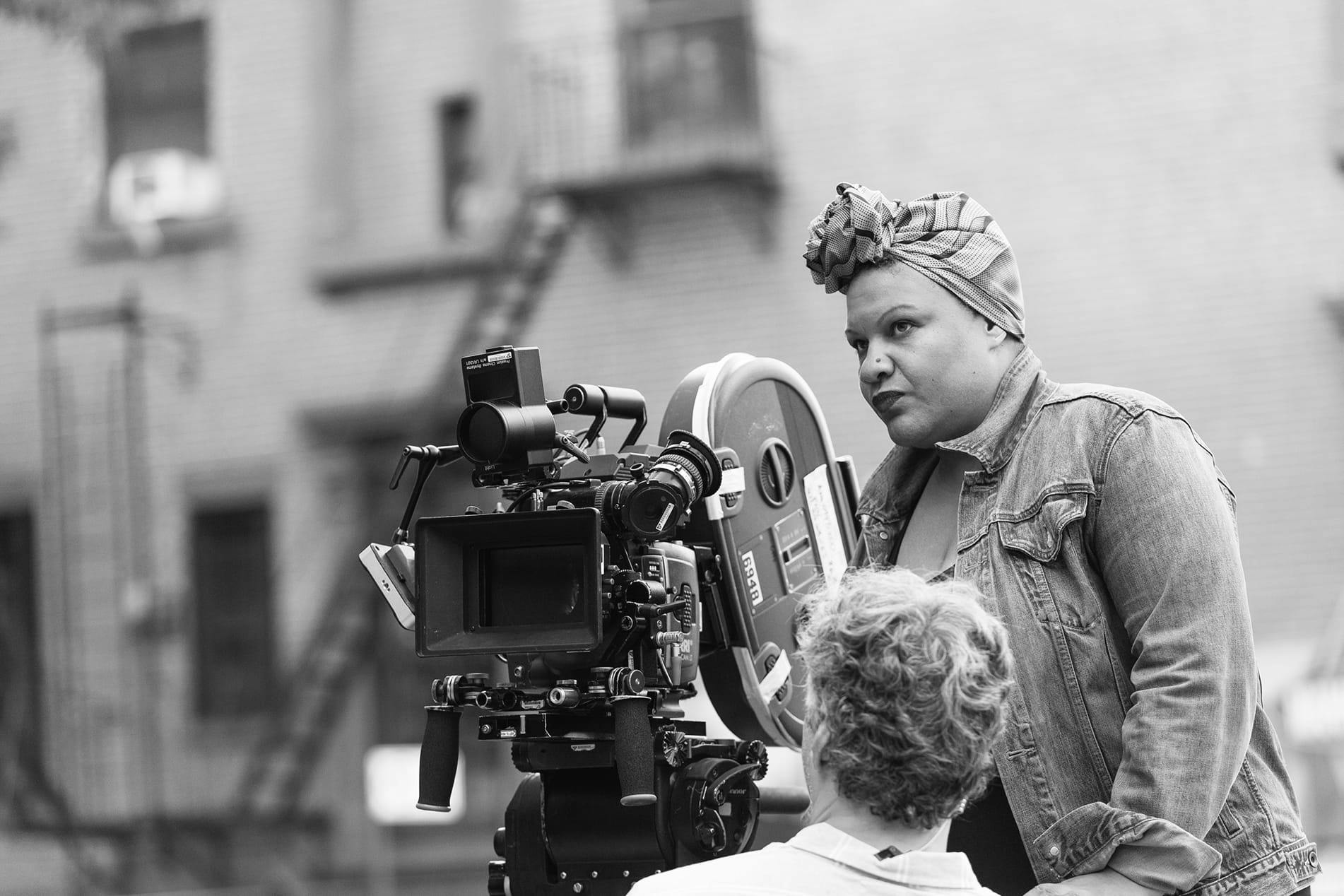 Black and white image shows writer-director Radha Blank behind the camera on set.