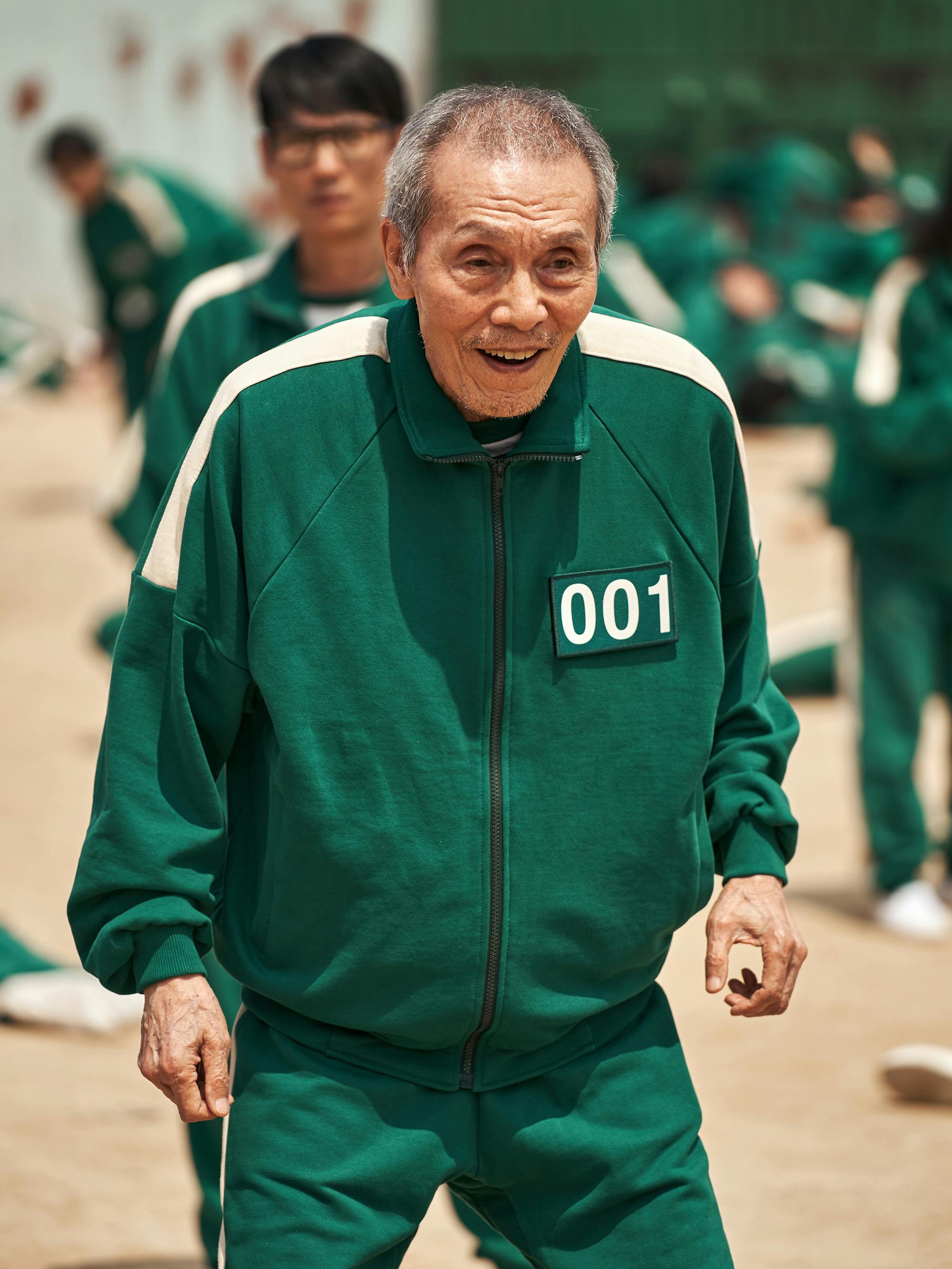 Oh Il-nam (Oh Young-soo) wears a 001 green tracksuit and smiles.