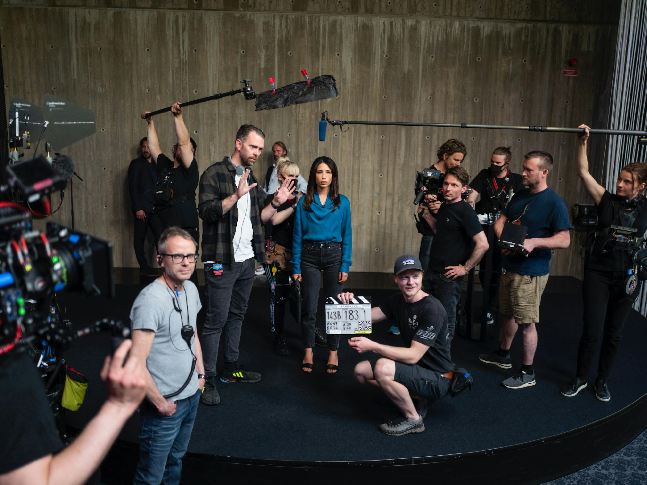 The cast and crew on the set of Snabba Cash. Evin Ahmad stands at the center in a teal shirt. There are cameras all around her.