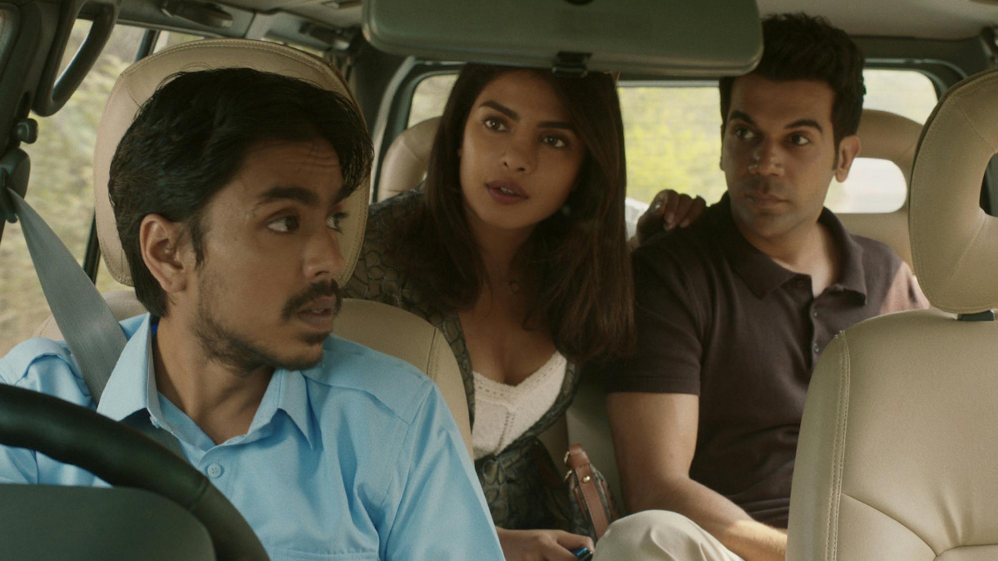 Balram (Adarsh Gourav), Pinky Madam (Priyanka Chopra Jonas) and Ashok (Rajkummar Rao) are inside a car. Balram is driving while Pinky and Ashok sit in the backseat. They are looking towards Balram who appears to be speaking to them from the front of the car. The interiors are covered in a nice cream leather. 