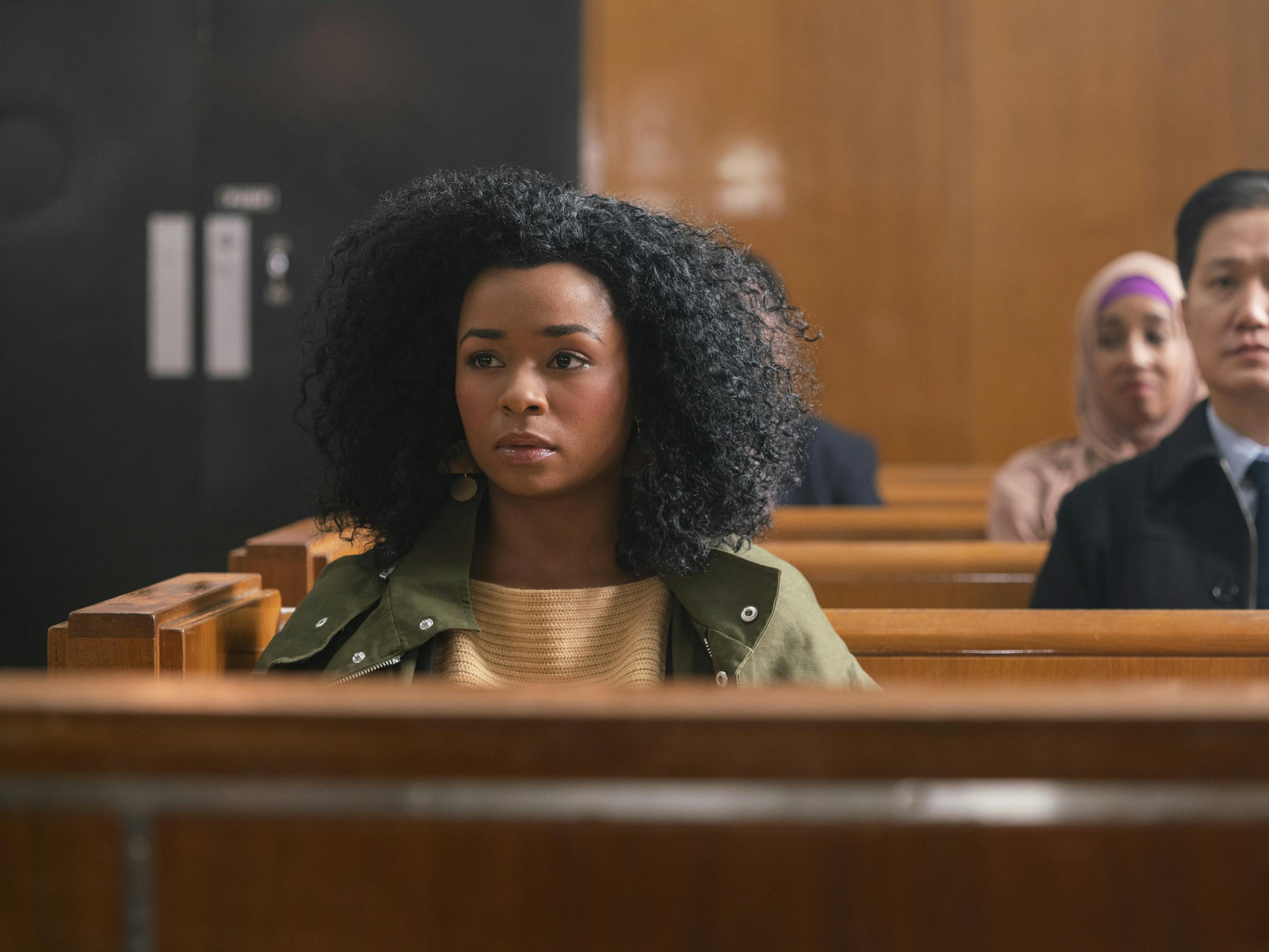 Alexis Floyd wears a white top and green jacket as she sits in a courtroom pew.