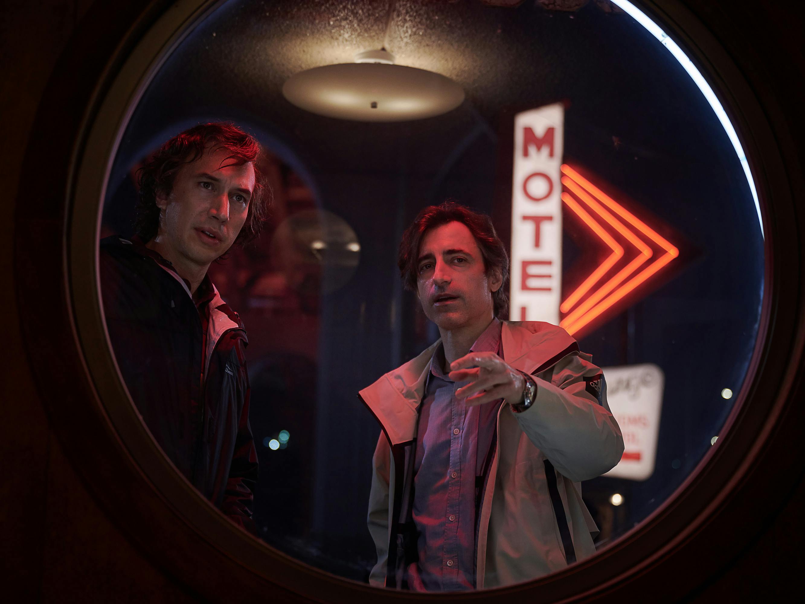 Adam Driver and Noah Baumbach look through a circular opening. behind them is a neon motel sign.