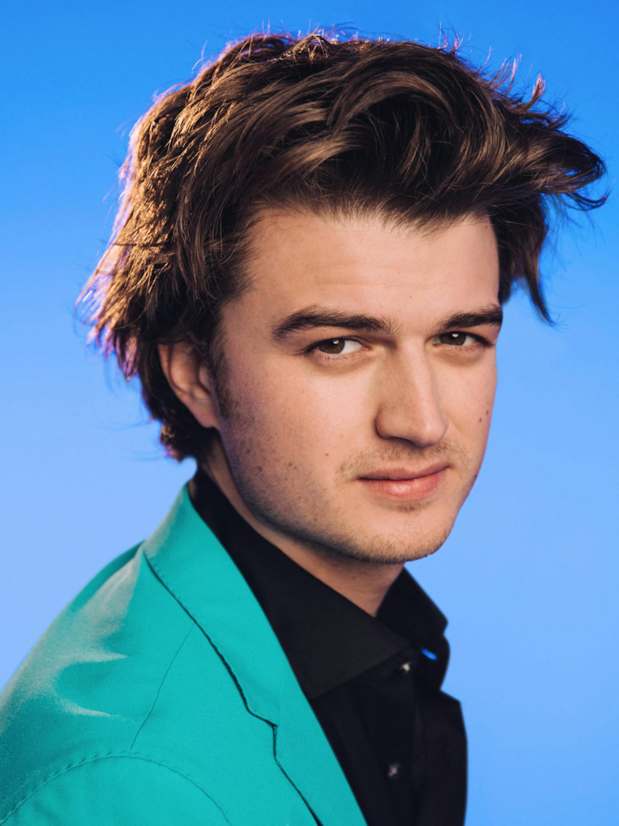 A close-up of Joe Keery of Stranger Things in front of a sky blue background.