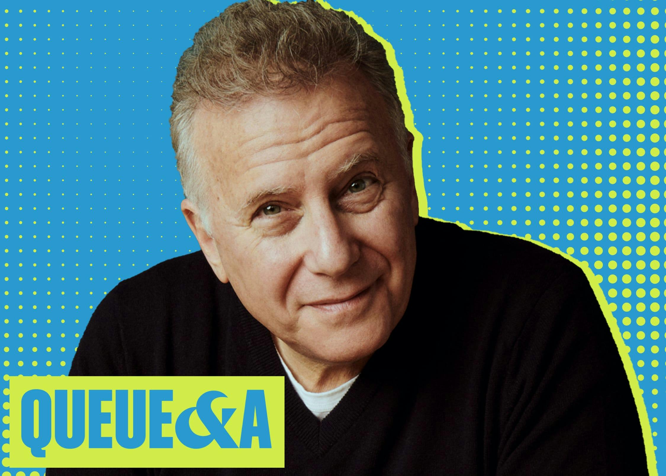 Paul Reiser wears a black sweater. The background is blue and yellow, and it reads Queue & A in the bottom left hand corner.