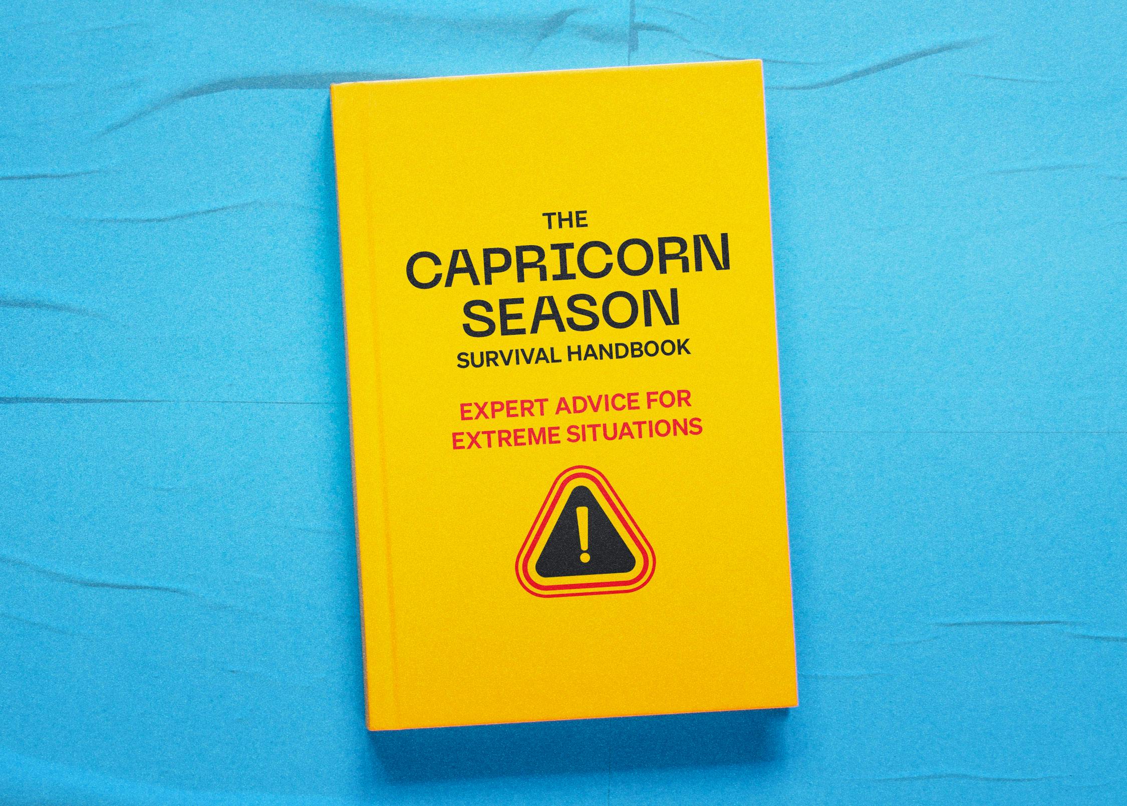 A yellow book titled "The Capricorn Season Survival Handbook Expert Advice for Extreme Situations" lies on a bright blue background.