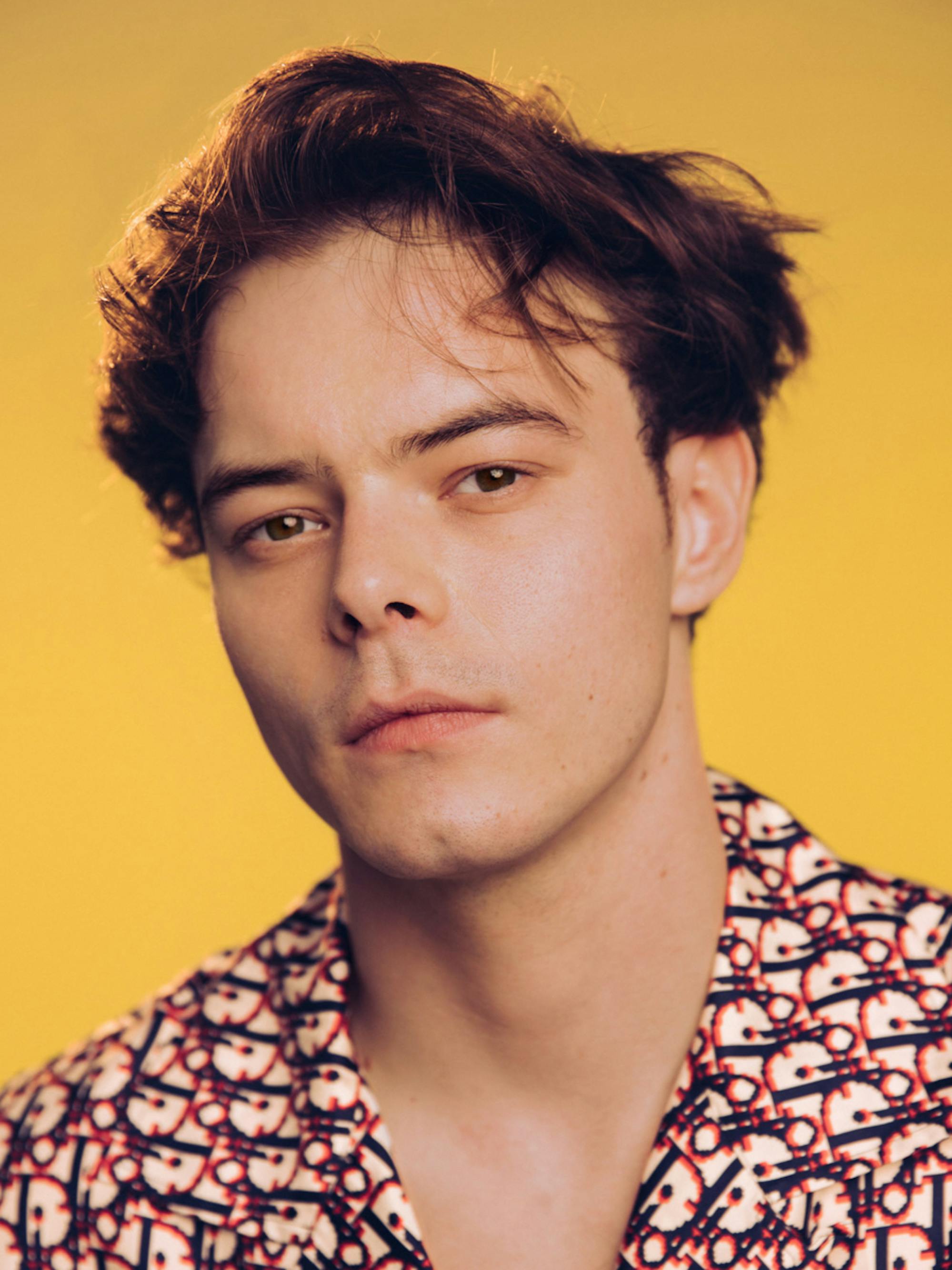 A close-up of Charlie Heaton of Stranger Things in front of a mustard yellow background.