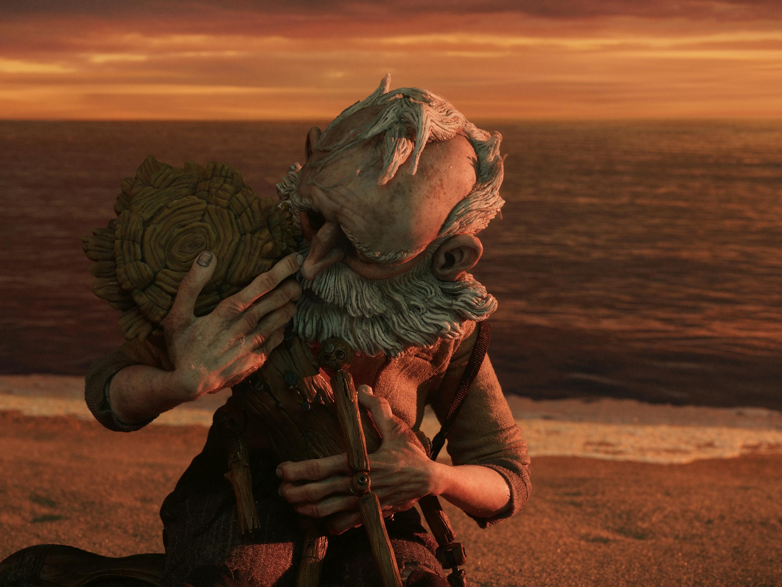 Geppetto (David Bradley) holds Pinocchio (Gregory Mann) in his arms on a sunset-lit beach.