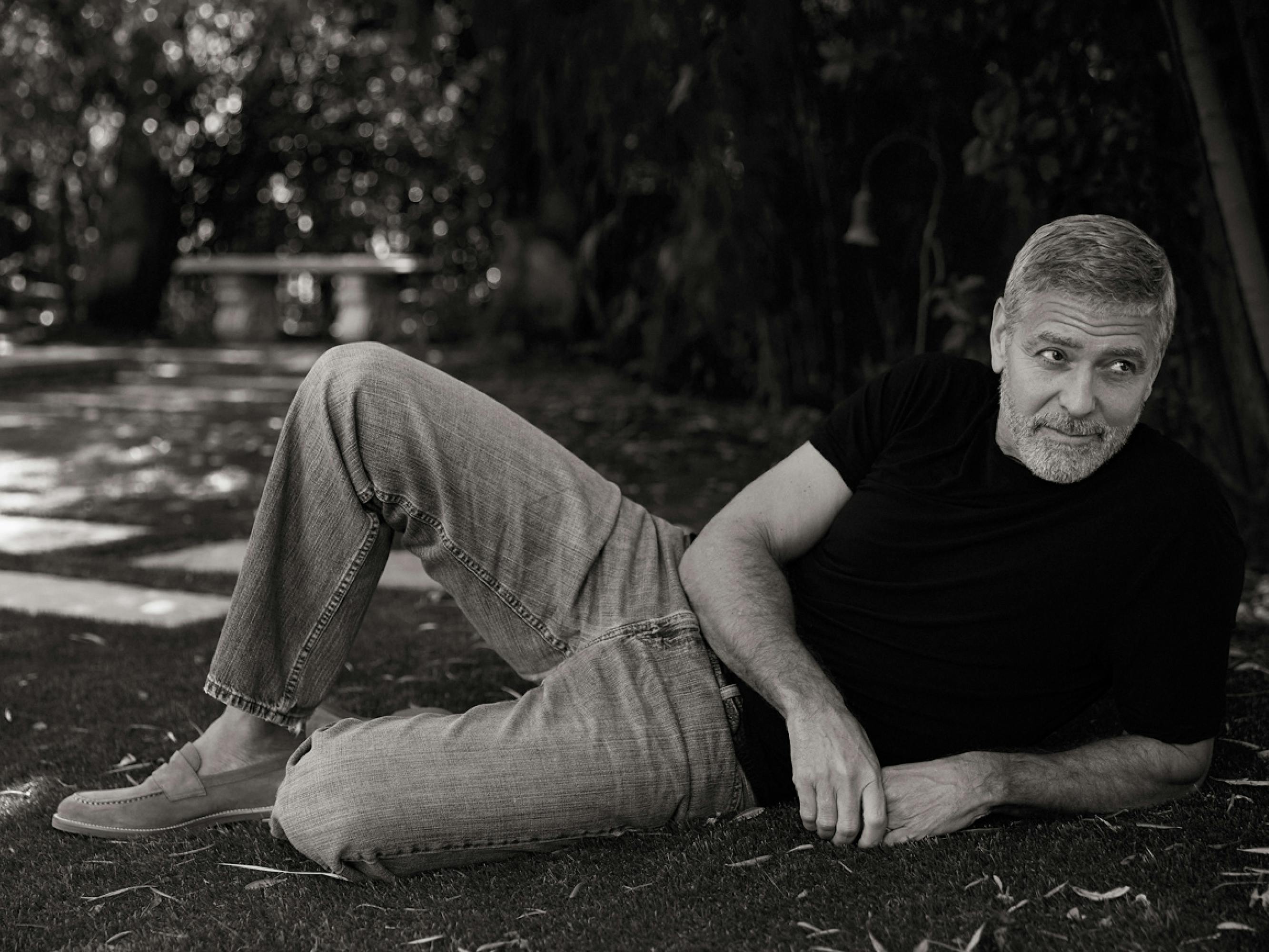 George Clooney shot in black-and-white, lounging on his lawn. He looks off into the distance. 