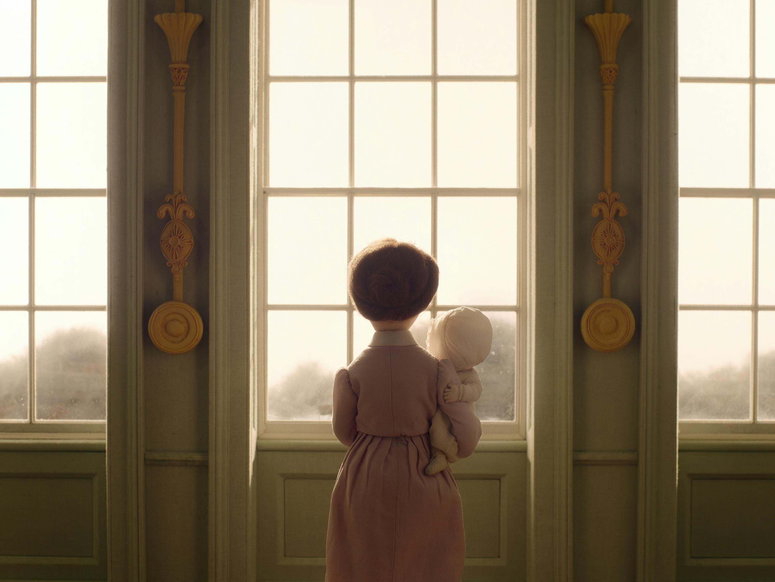 A felt woman holds a felt baby and looks out through a triptych window.