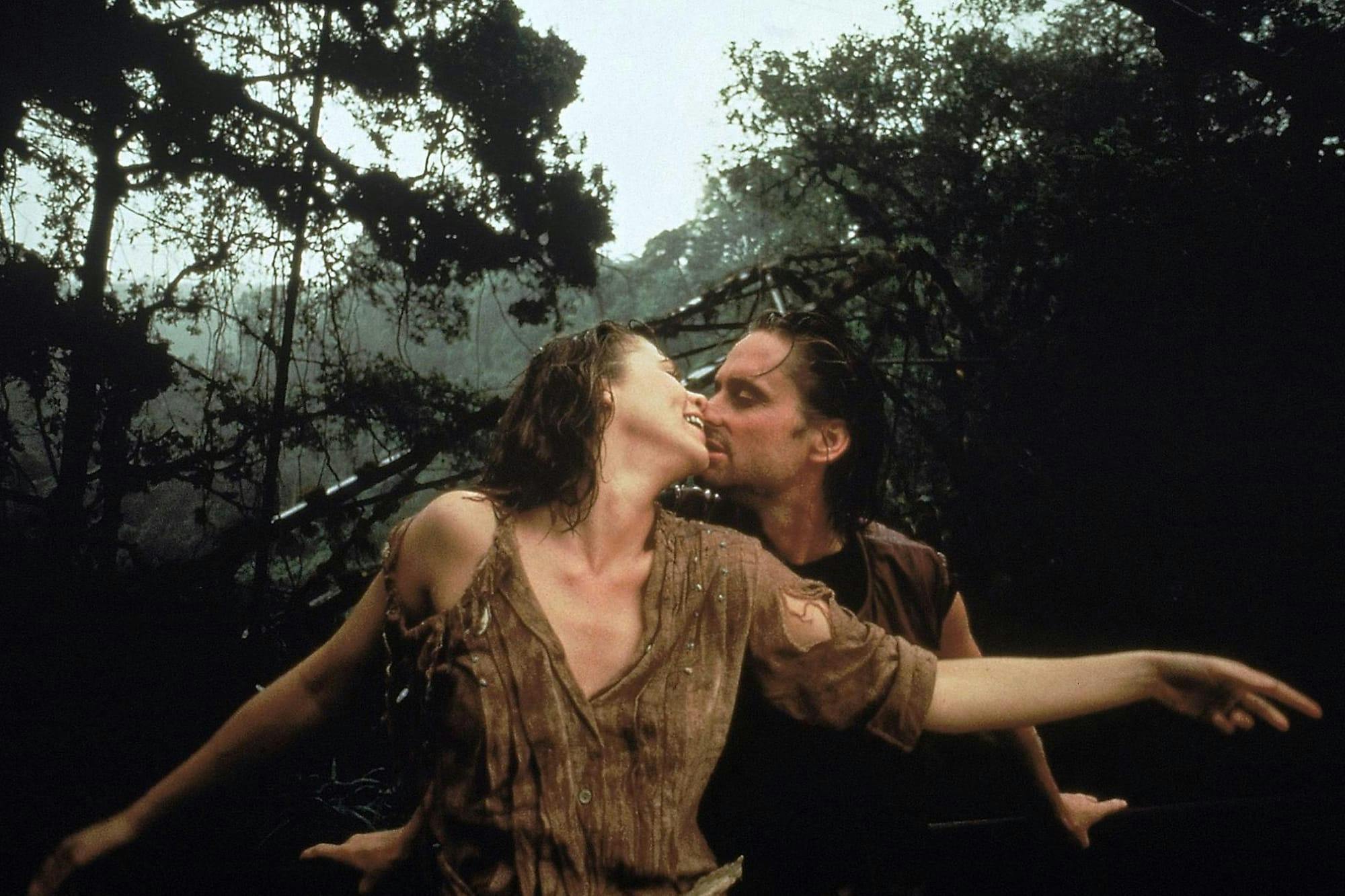 Joan Wilder (Kathleen Turner) and Jack T. Colton (Michael Douglas) in Romancing the Stone. The wear neutral clothing and embrace in the middle of the woods.