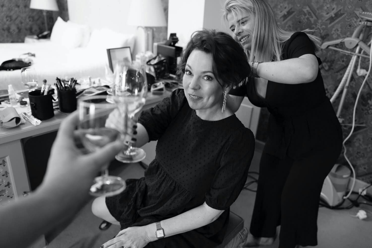 Olivia Colman gets ready while enjoying a champagne toast at the Venice Film Festival, 2021 wearing a black jacket scoop neck. 