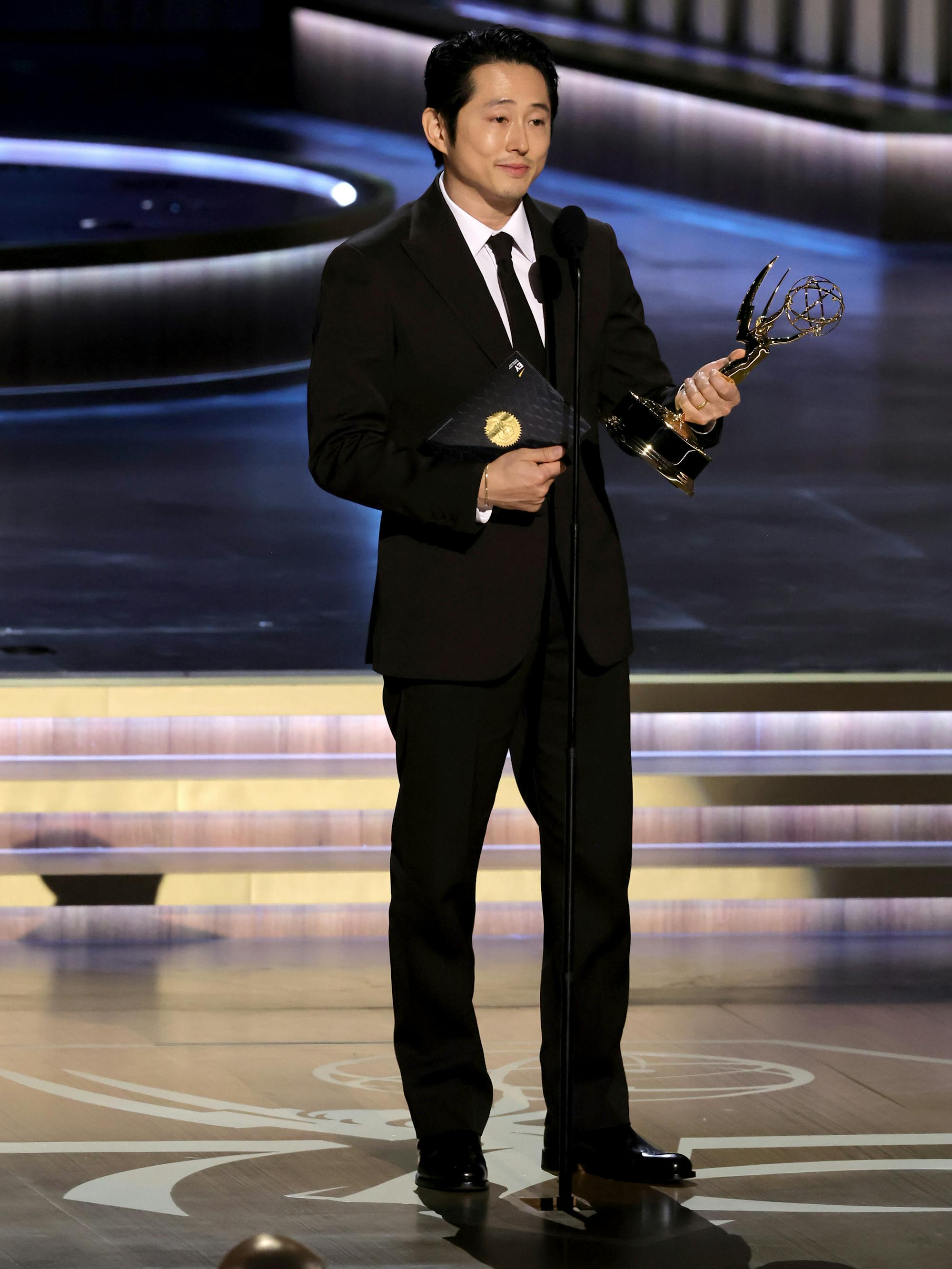 Steven Yeun wears a black tux and holds his Emmy onstage.