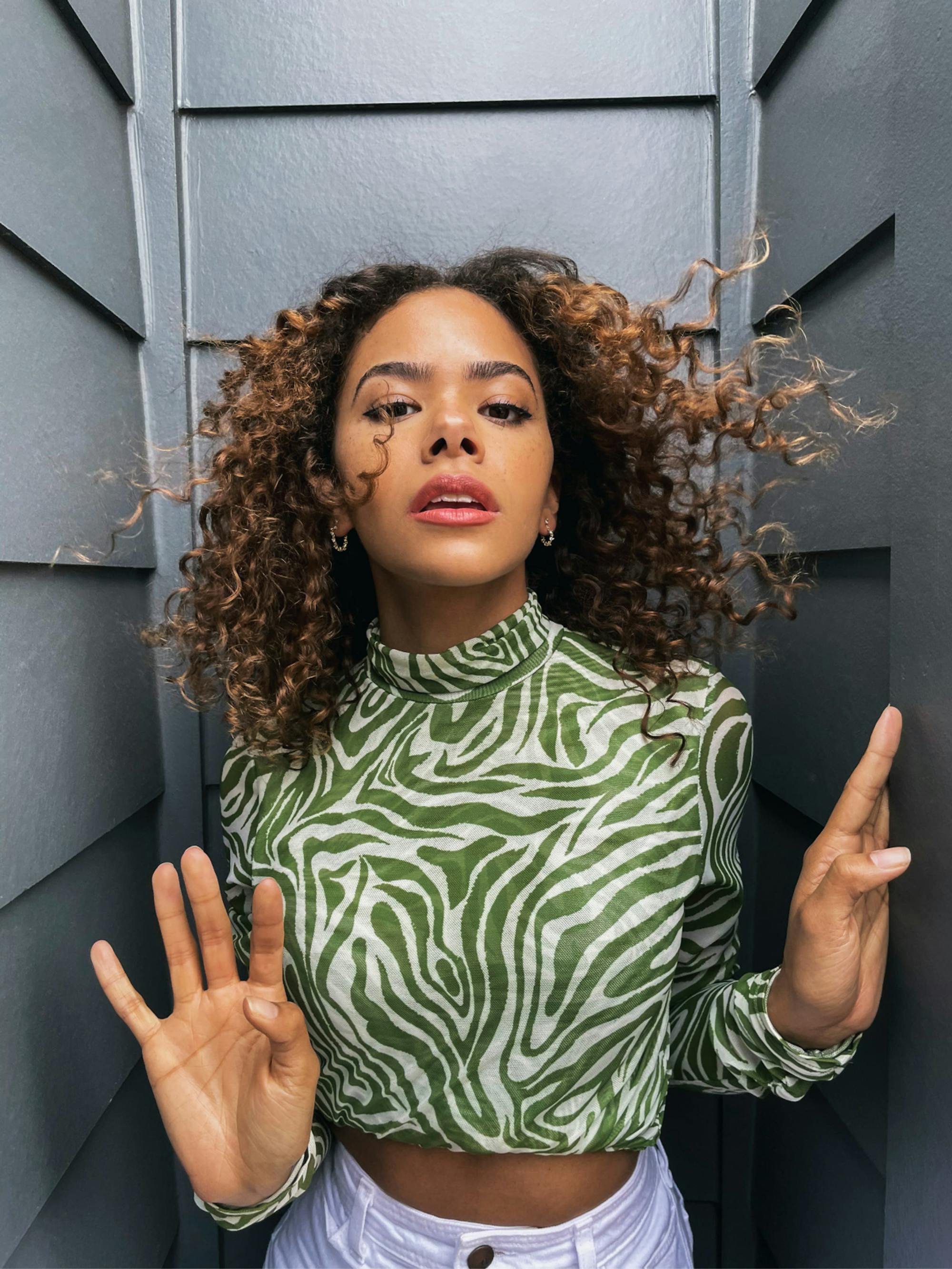 Antonia Gentry poses between two dark shingled walls, in a green zebra turtleneck.