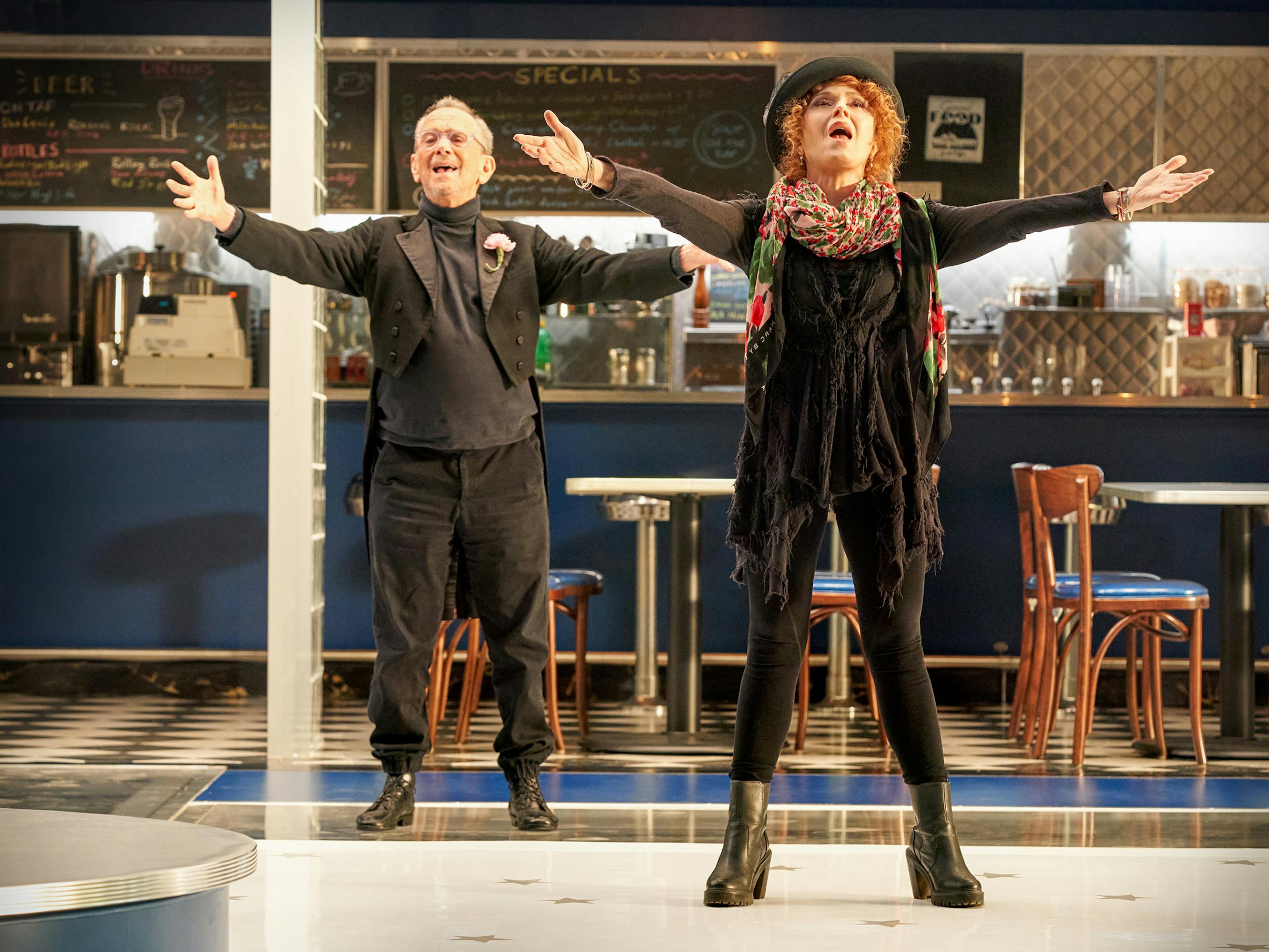 Joel Grey and Bernadette Peters wear all black and raise their arms in song.