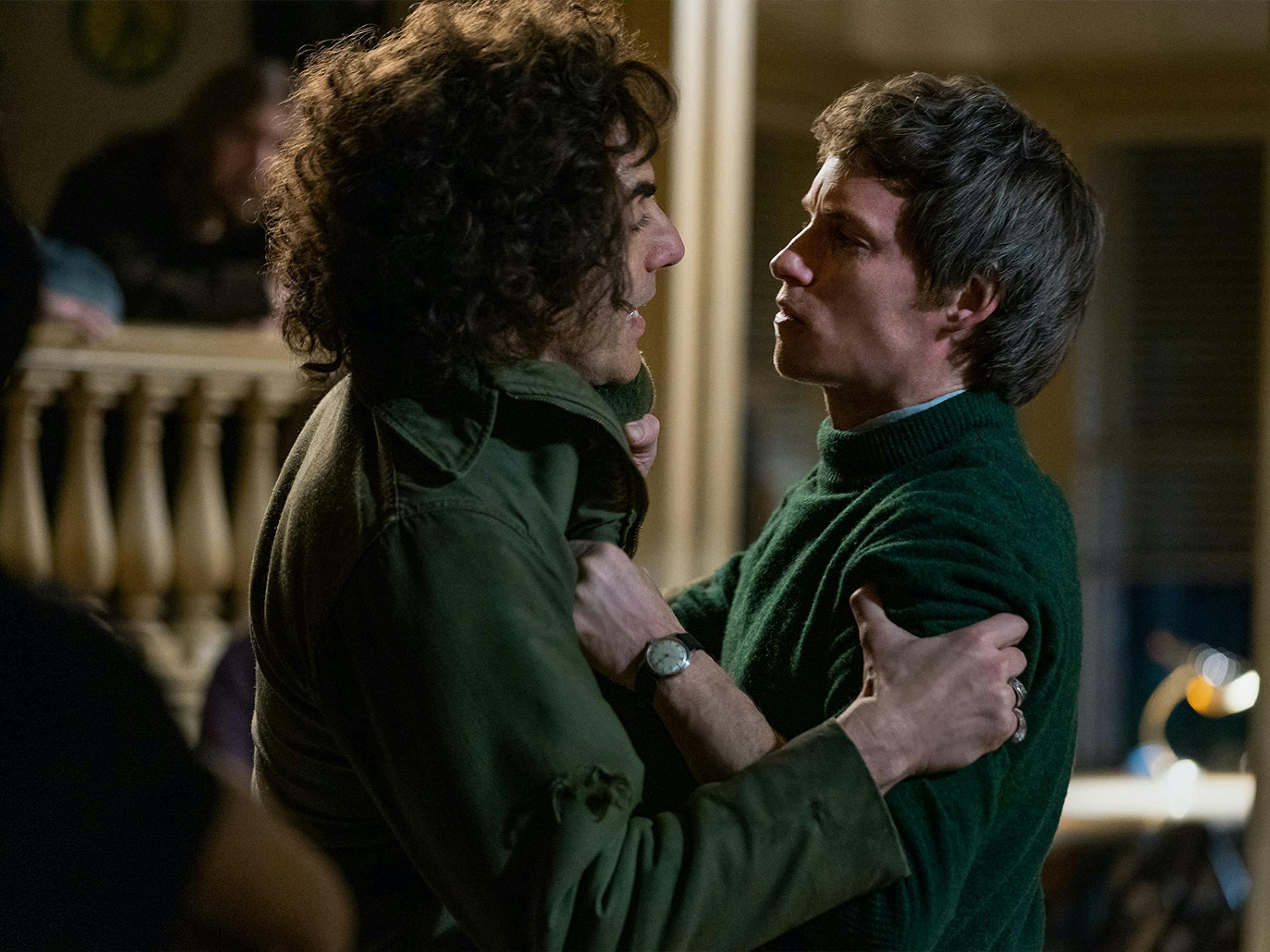 Cohen and Redmayne grip each other in a tense showdown. They both wear green, and look angry, while Cohen appears to be speaking.