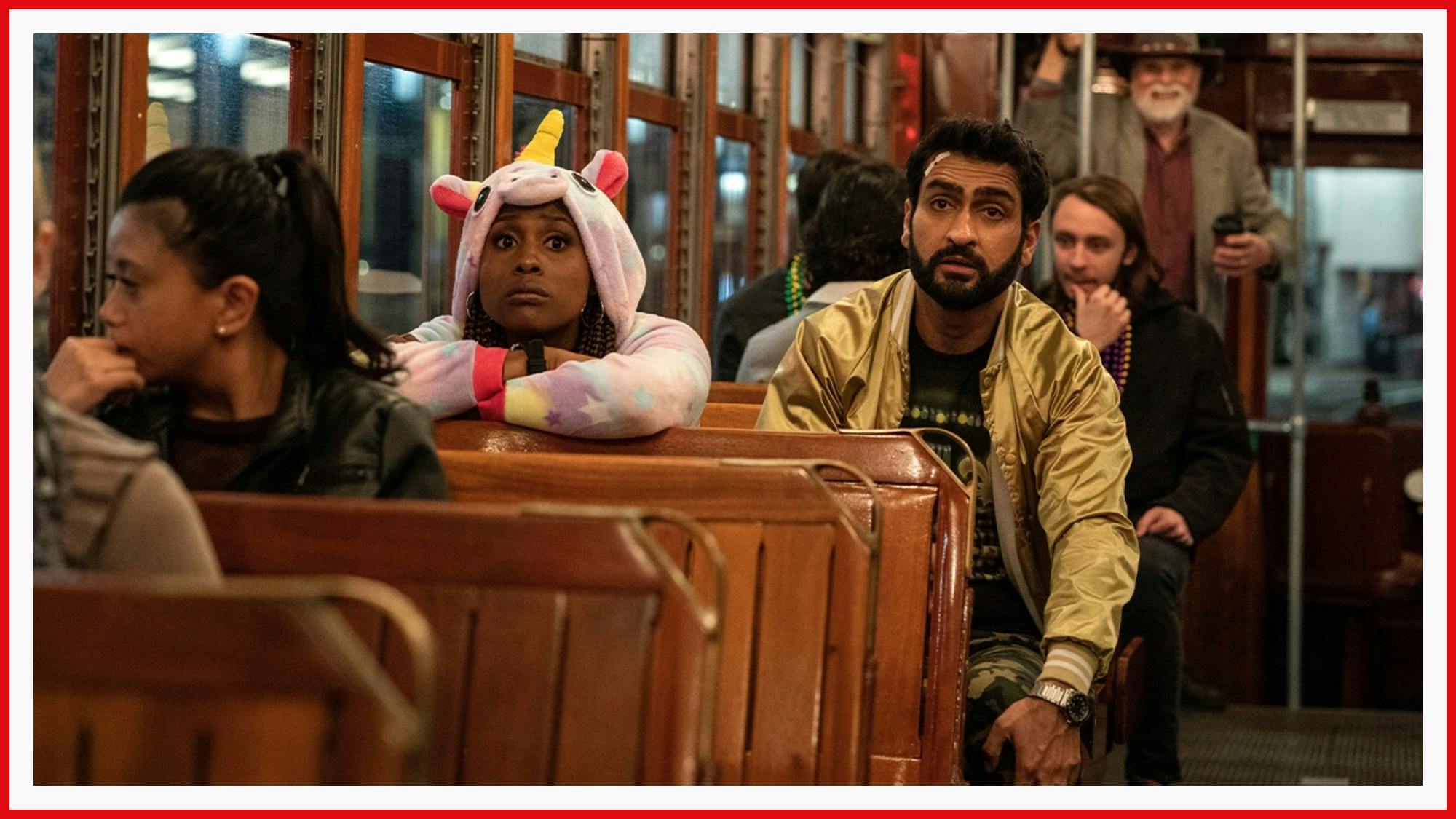 Kumail Nanjiani and co-star Issa Rae are pictured on a streetcar in The Lovebirds. Nanjiani sports a gold bomber jacket and Issa Rae is dressed to impress in a pink unicorn onesie.