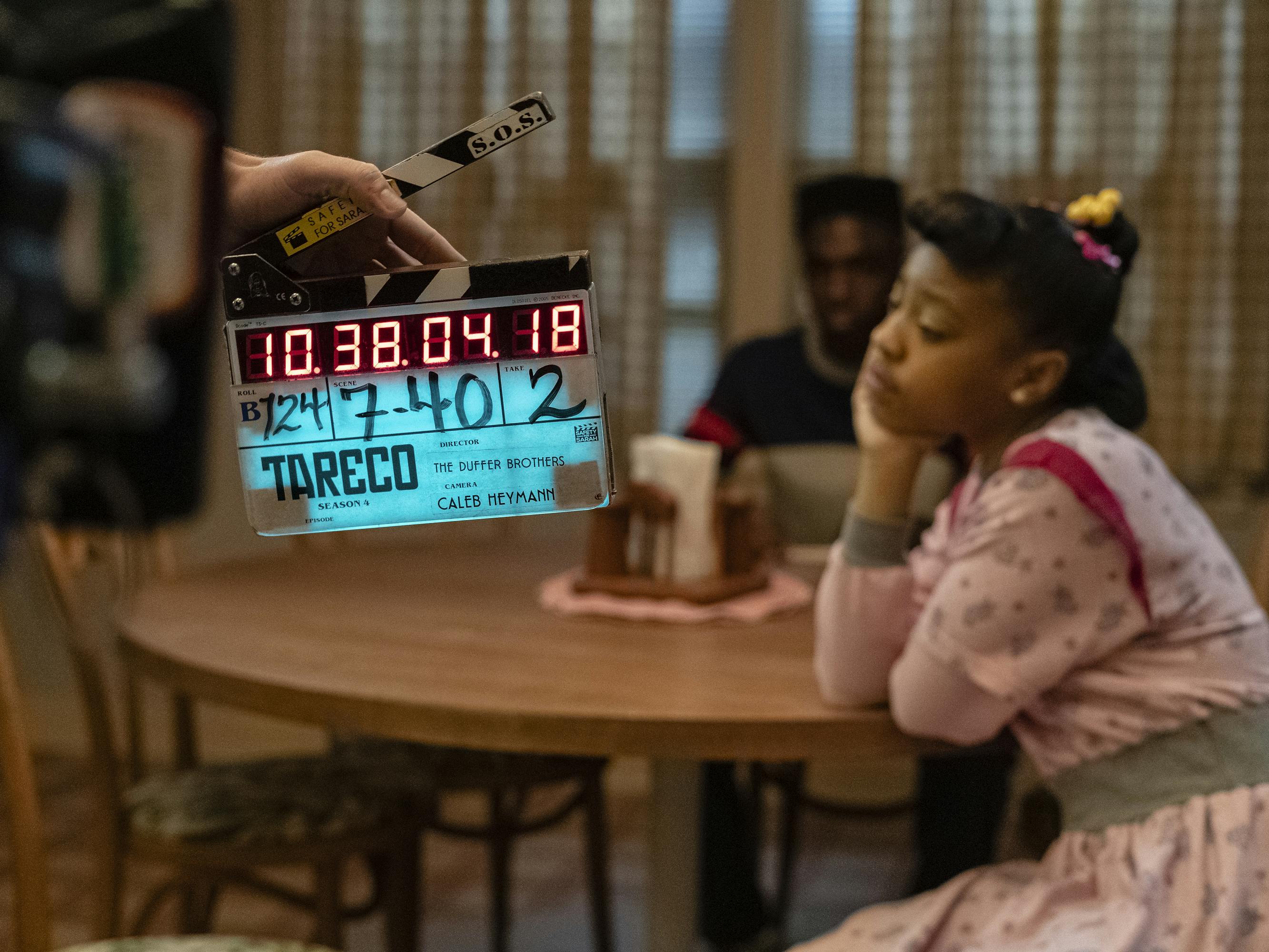 Erica Sinclair (Priah Ferguson) wears a pink dress and rests her chin in her palm on a wood table.