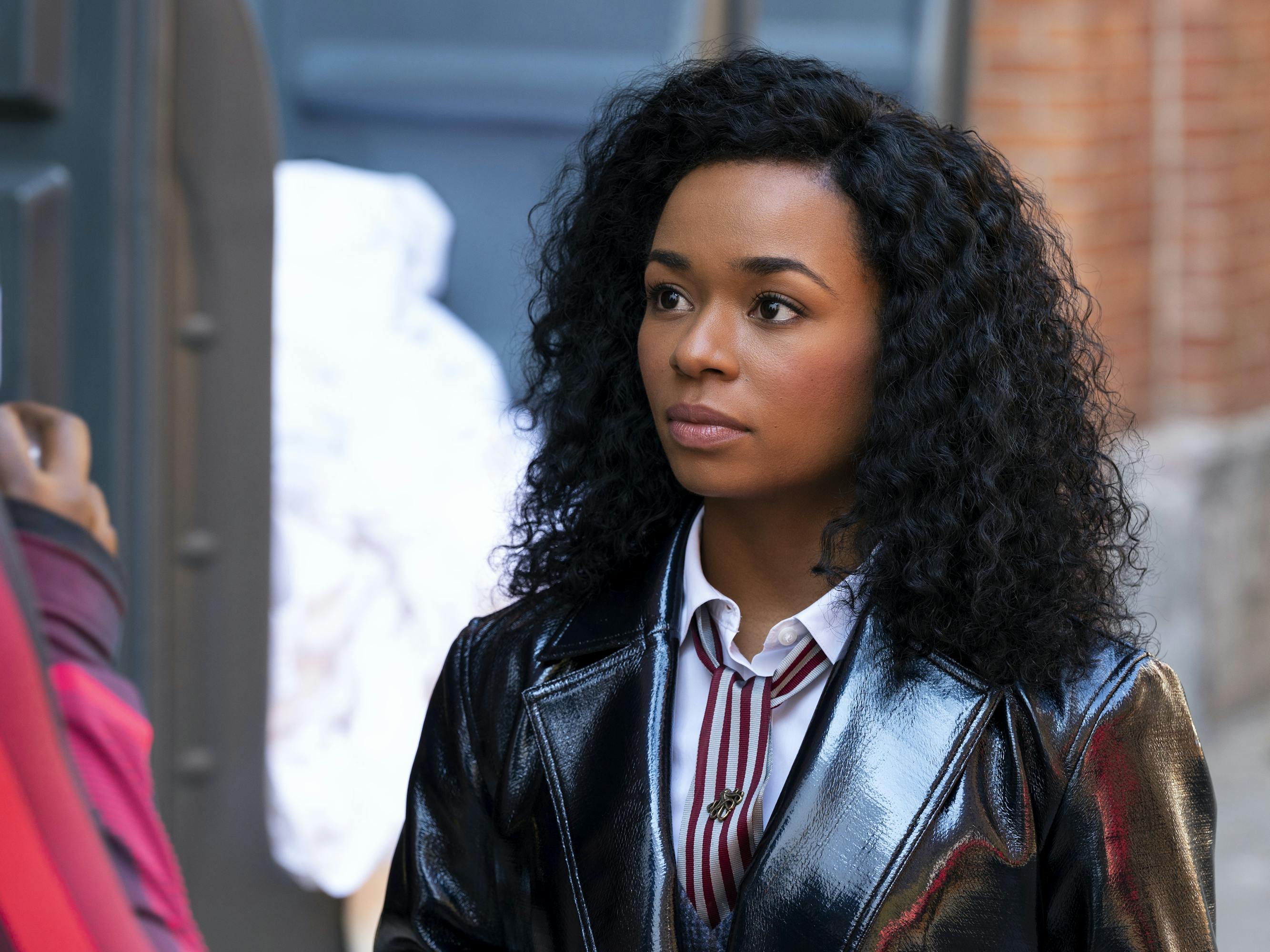 Neff (Alexis Floyd) wears a glossy leather jacket and stands outside against a brick wall.