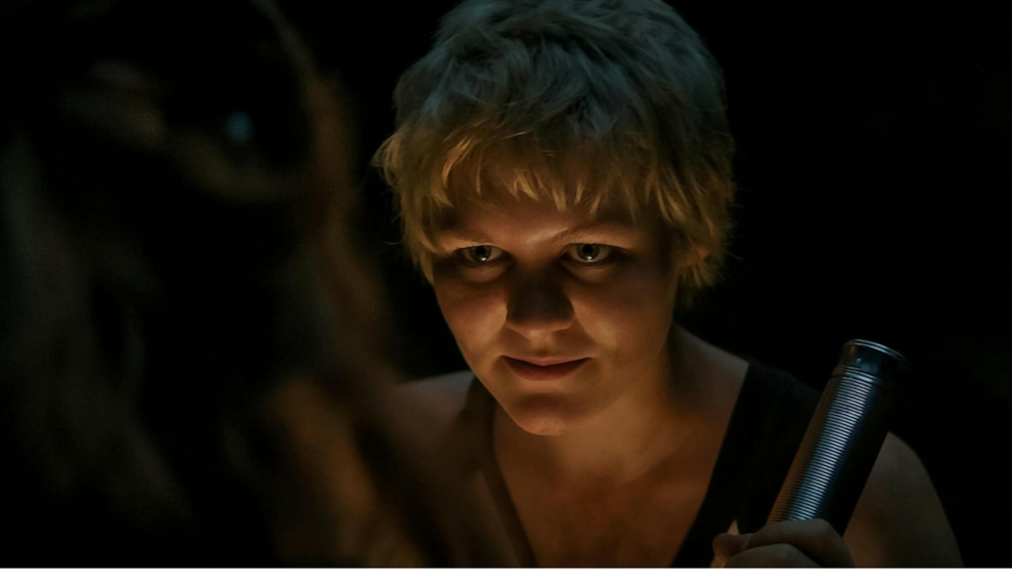 Alice (Ryan Simpkins) in a dark ominous shot. She holds some kind of silver weapon.