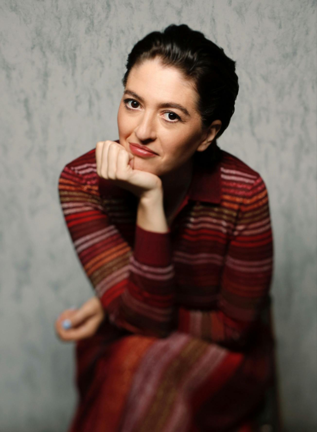 Marielle Heller sits with her head resting on her palm, in a striped sweater.