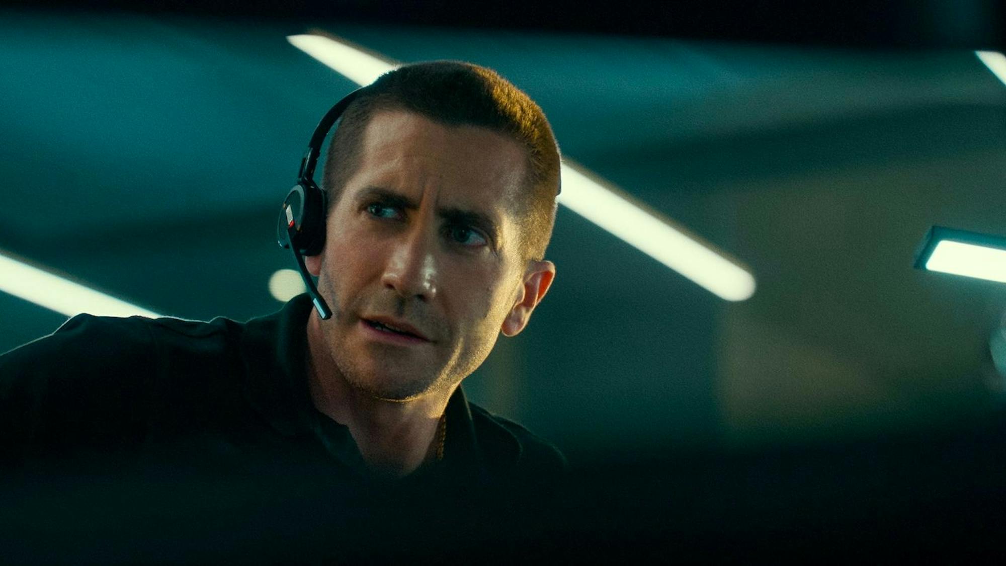 Joe Baylor (Jake Gyllenhaal) in The Guilty (2021) wears a dark polo shirt and a headset.