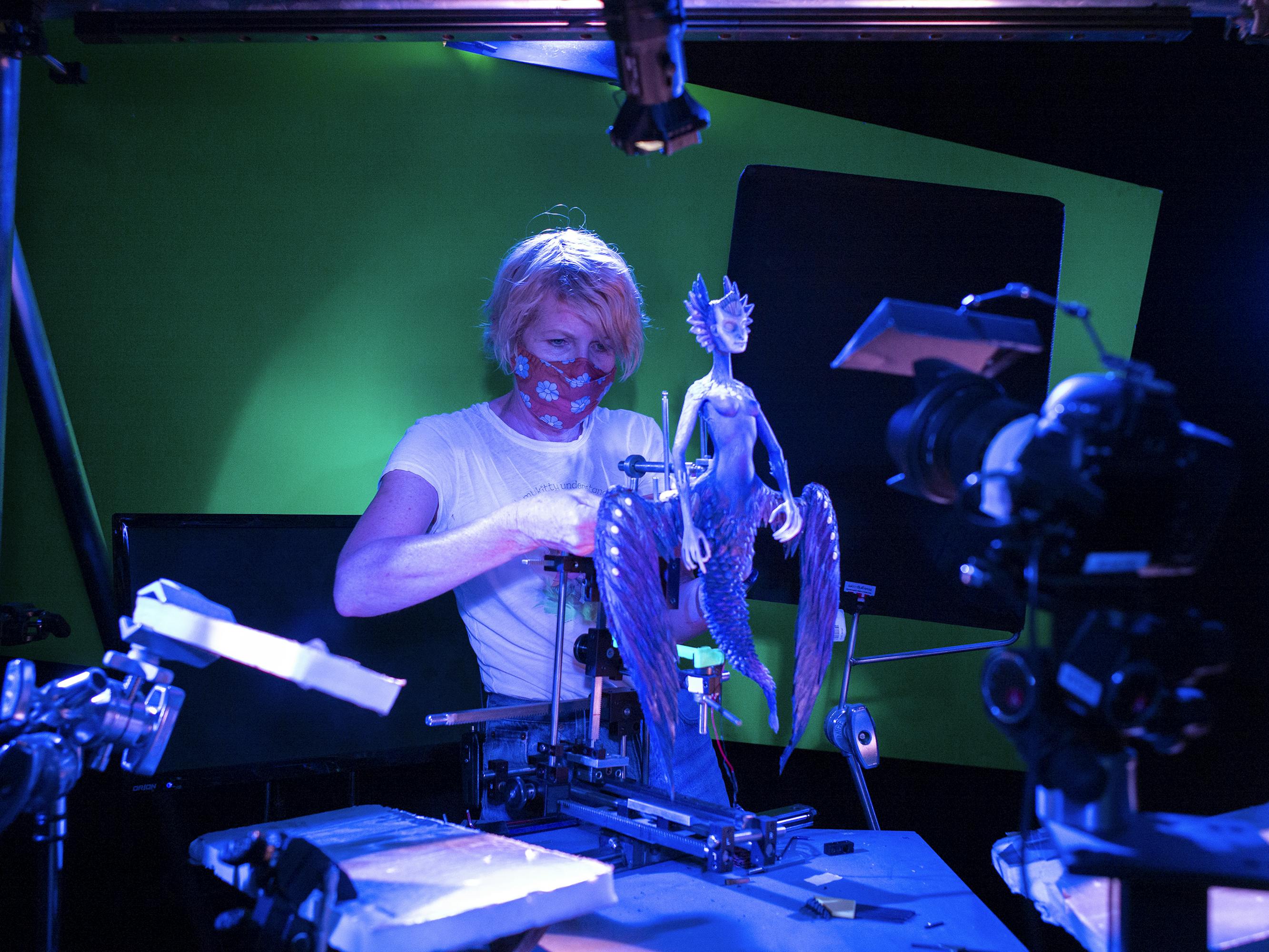 An artist works on a Death puppet in a blue lit studio with green walls