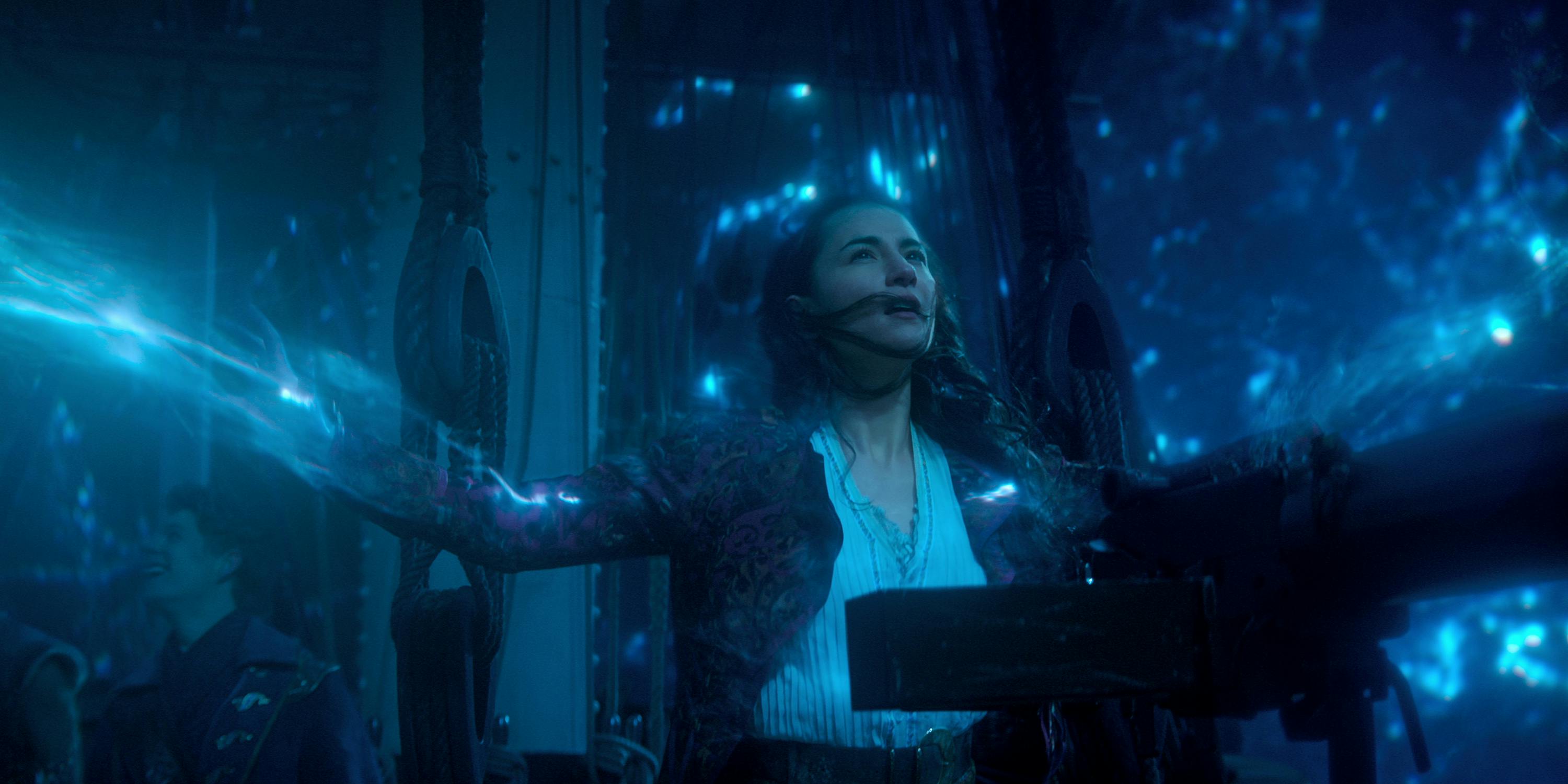 Alina Starkov (Jessie Mei Li) stands in a dark room surrounded by neon blue light. 