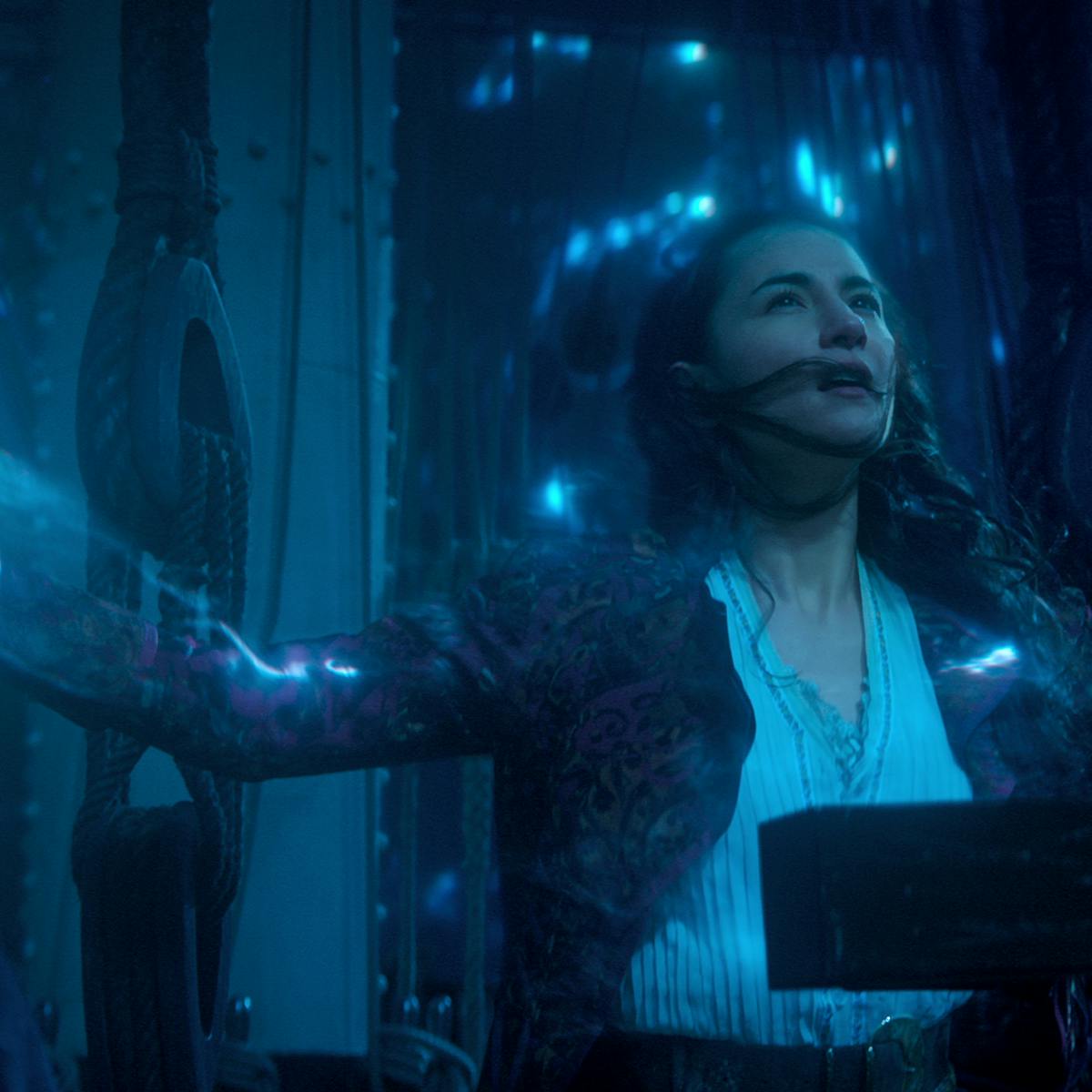 Alina Starkov (Jessie Mei Li) stands in a dark room surrounded by neon blue light. 