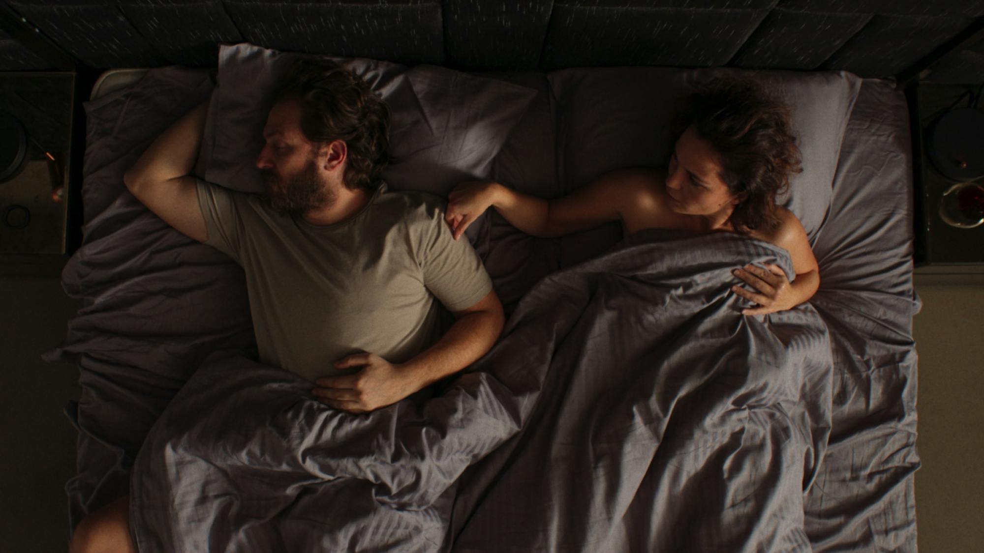 Sinan and Gülbin are pictured in bed, with their gray blankets pulled over them.
