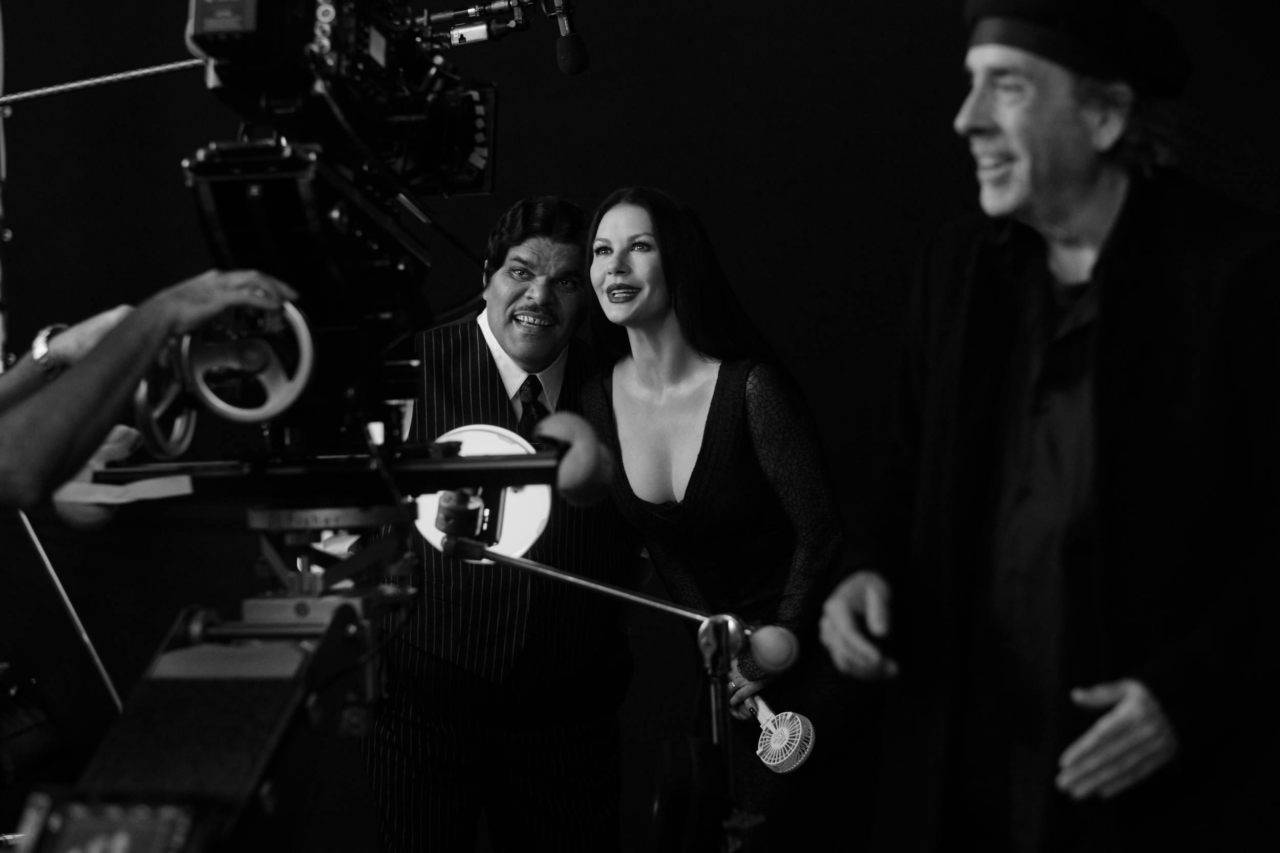 Luis Guzmán and Catherine Zeta-Jones crouch together in costume, and Tim Burton directs the camera from the side .