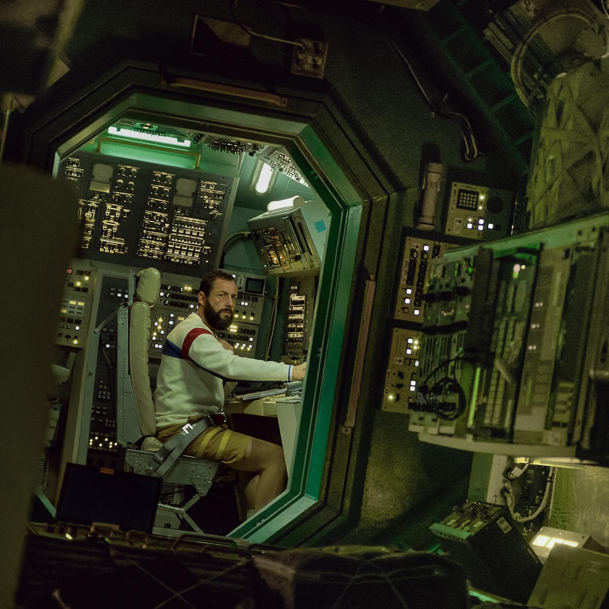 Jakub (Adam Sandler) works a console in a spaceship, lit by green light.