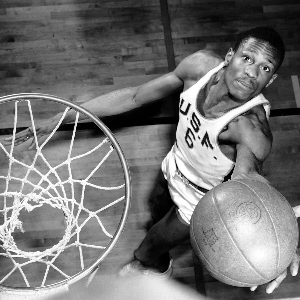 A black-and-white shot of Bill Russell from above, as he is about to lay the ball into the hoop.