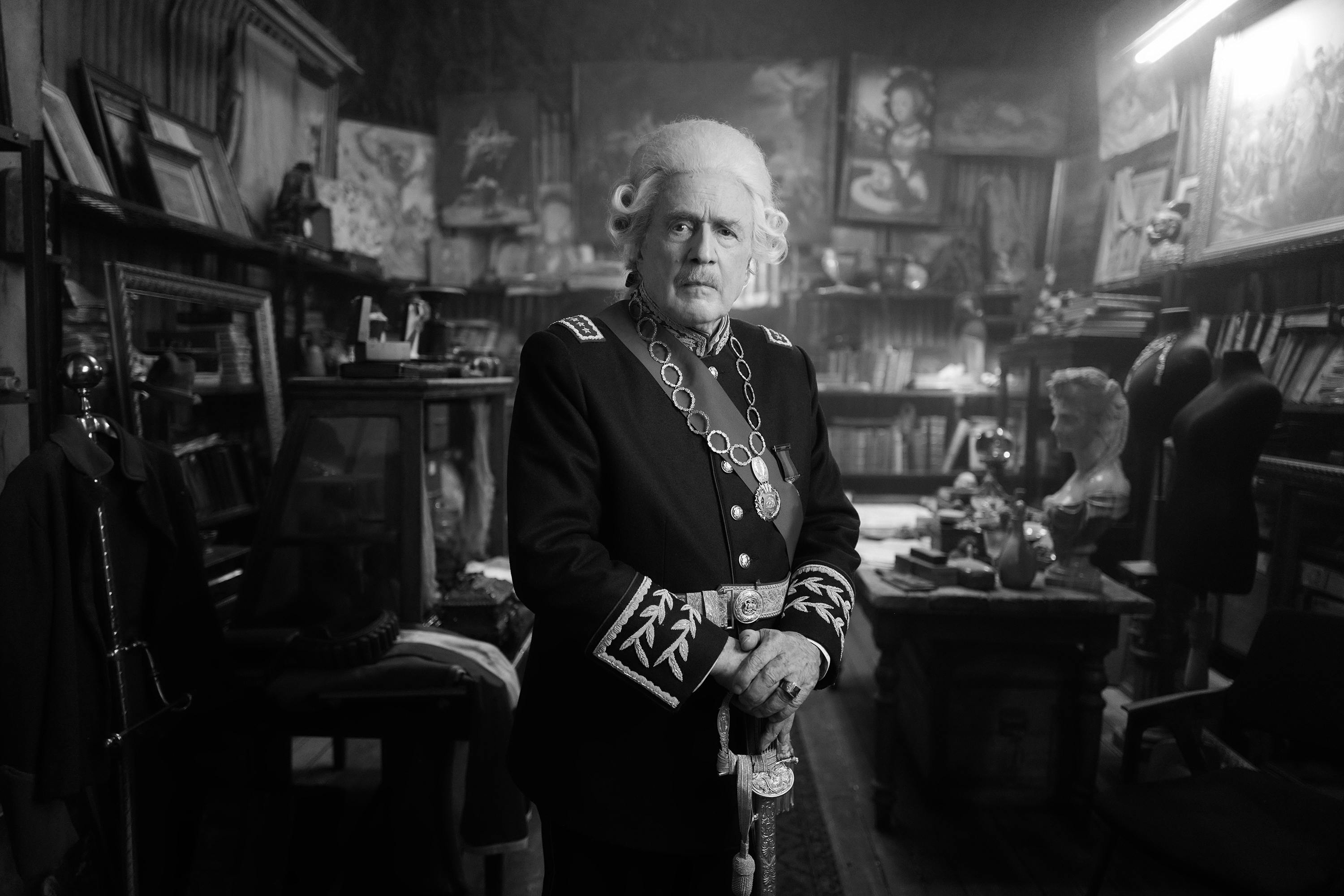 The Count (Jaime Vadell) in a black-and-white picture. He wears a uniform and stands in an office filled with books.