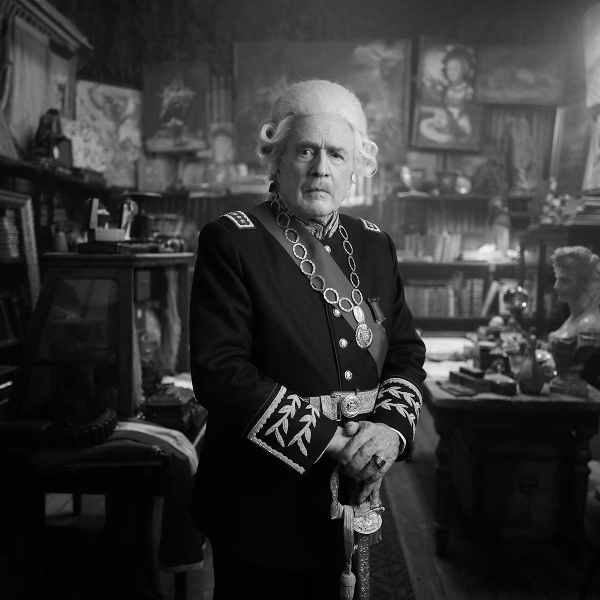 The Count (Jaime Vadell) in a black-and-white picture. He wears a uniform and stands in an office filled with books.