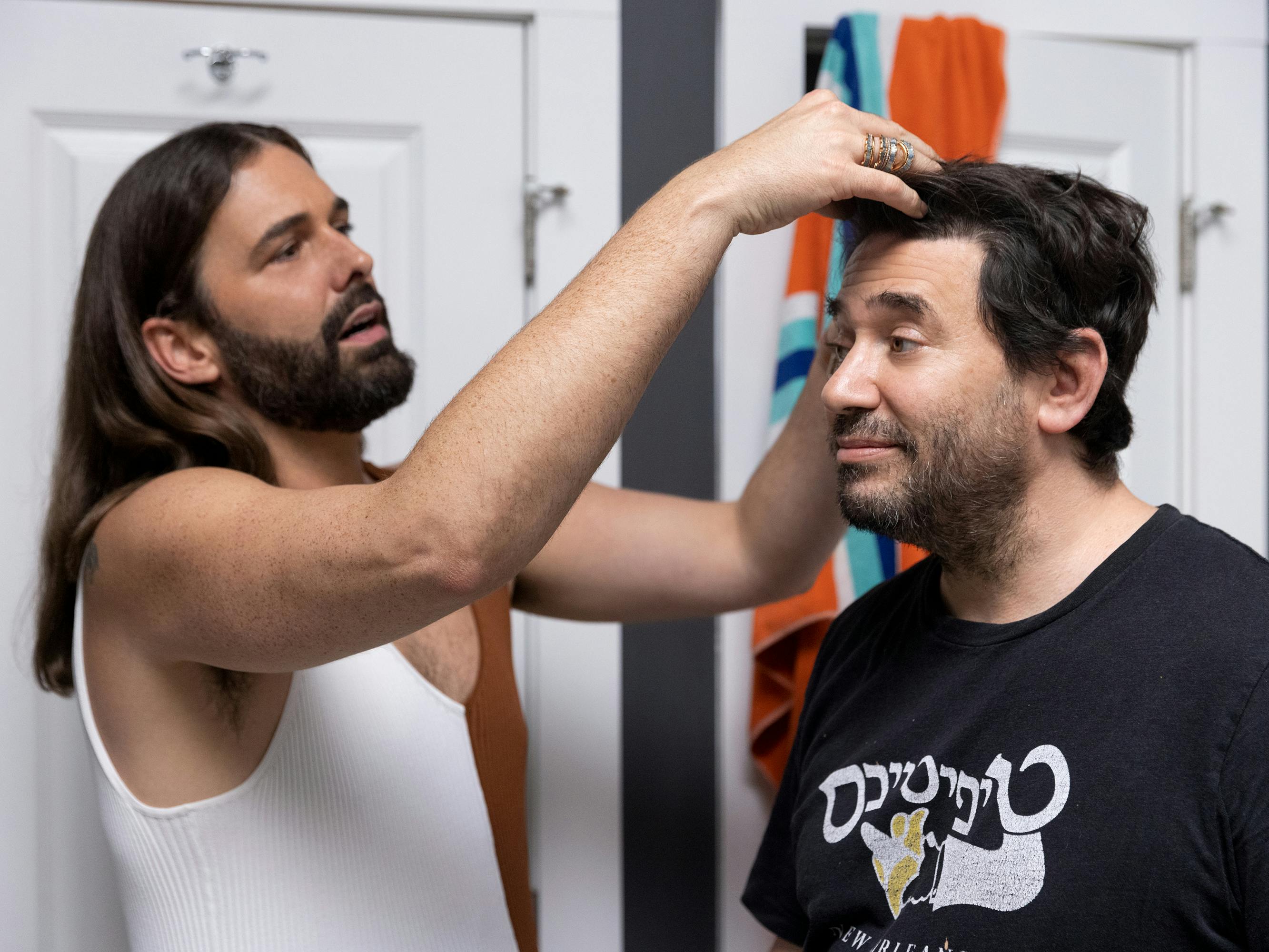 Jonathan Van Ness looks at Dan Stein's hair in a dark-walled bathroom.