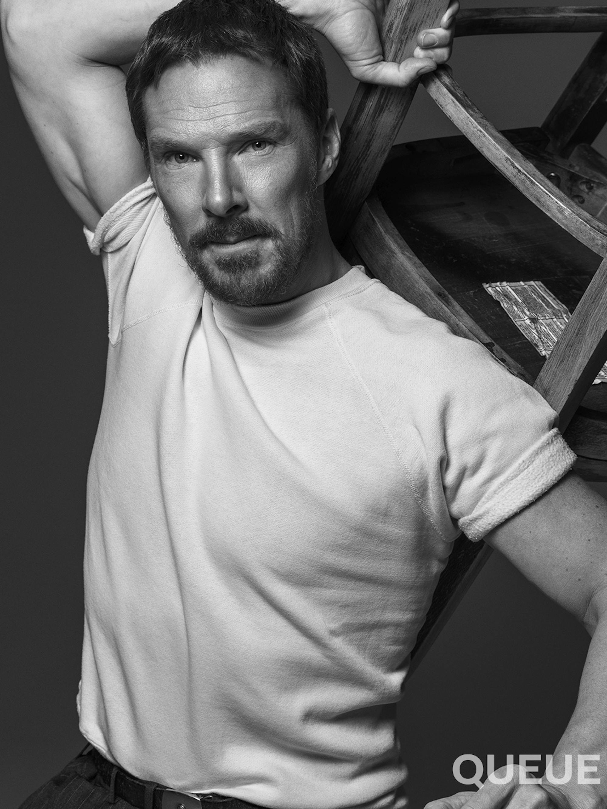 Benedict Cumberbatch wears a white t-shirt and holds a chair over his head. 