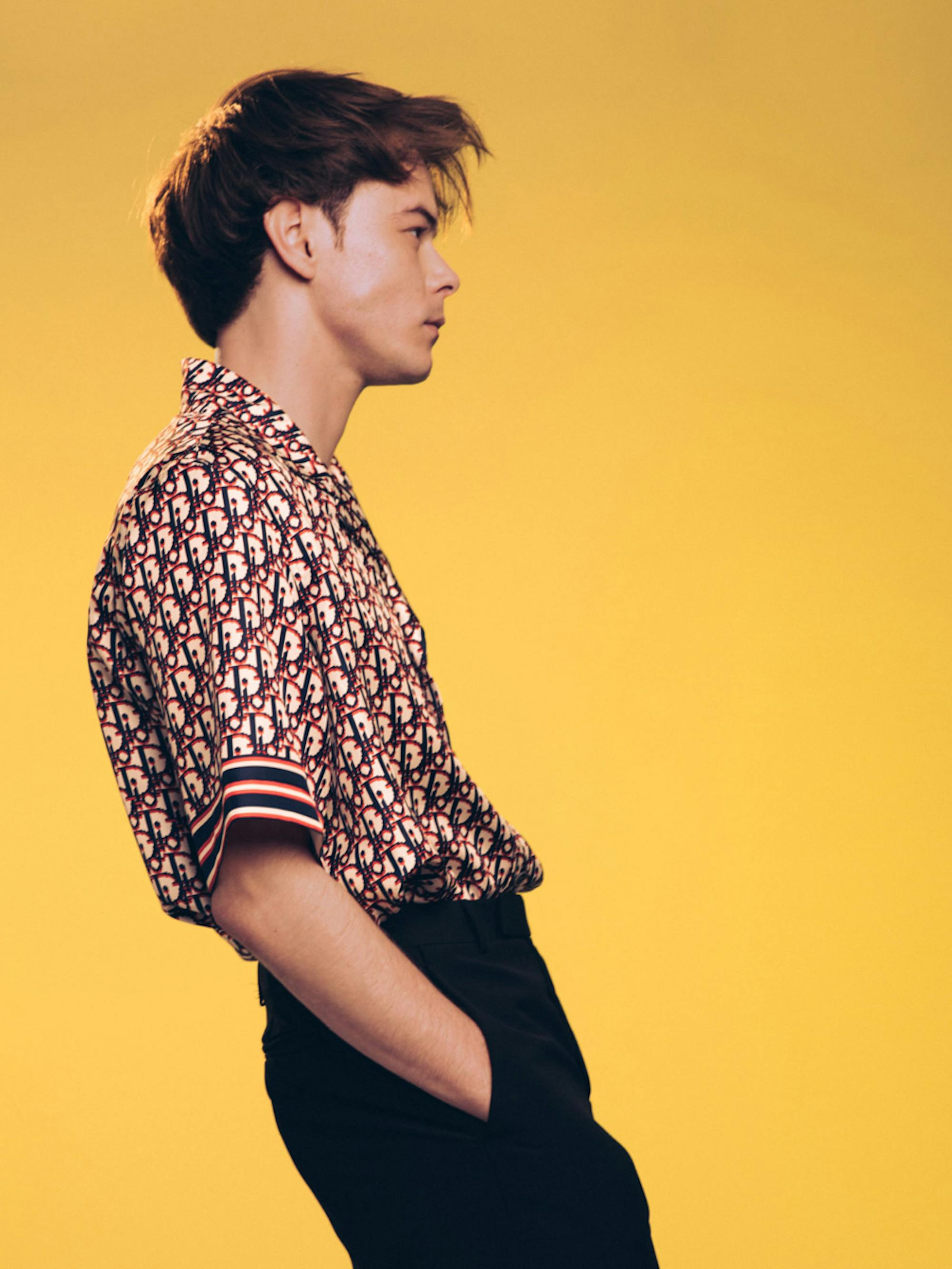 Charlie Heaton of Stranger Things poses in front of a mustard yellow background.