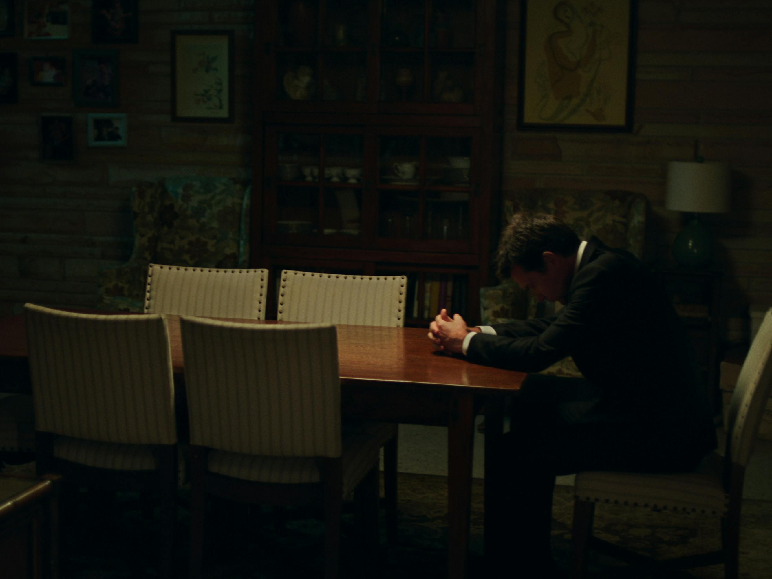 Marty Byrde (Jason Bateman) wears a tux and rests his head on a wood table surrounded by light beige chairs. 