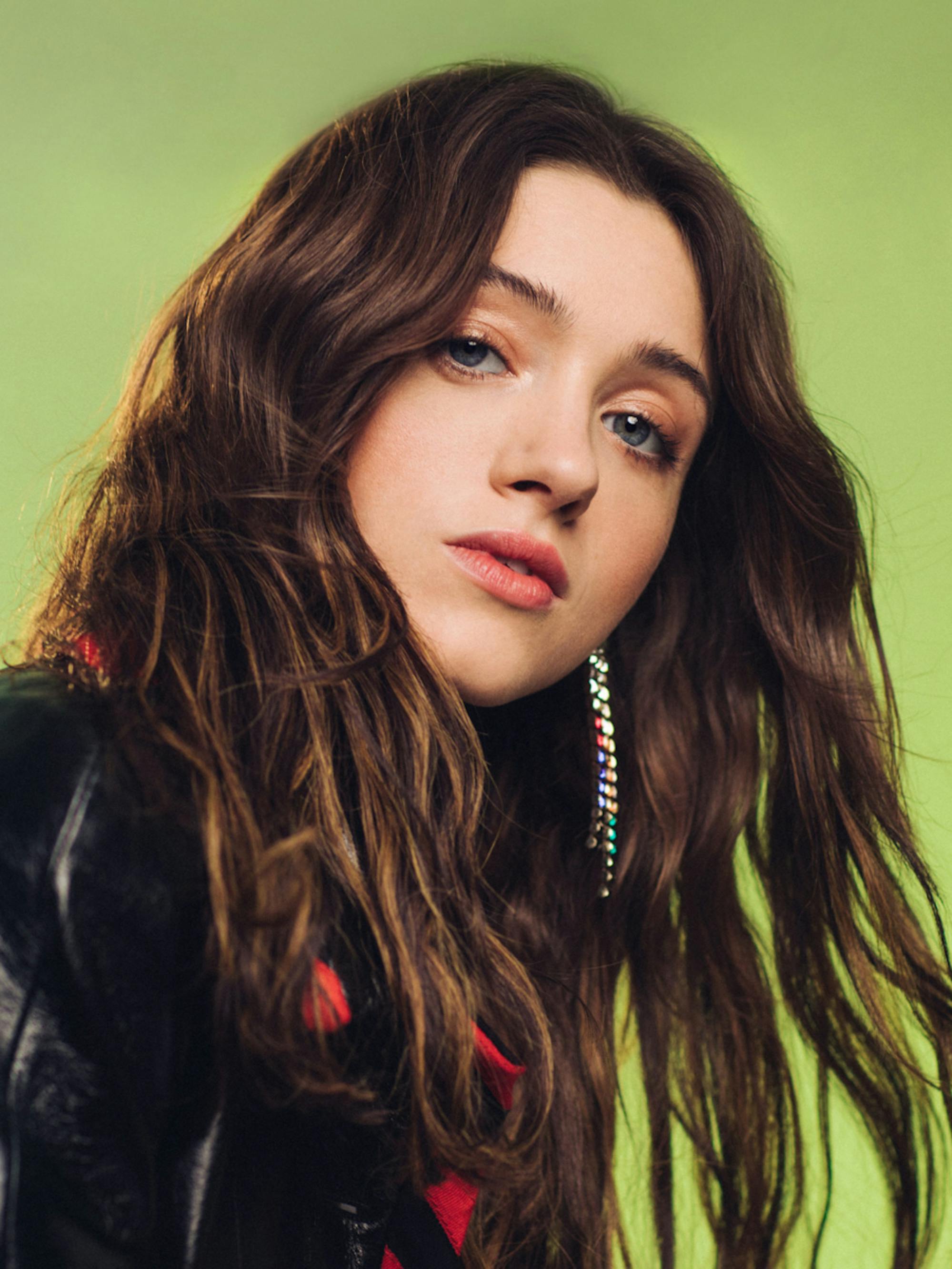 A close-up of Natalia Dyer of Stranger Things in front of a bright green background.