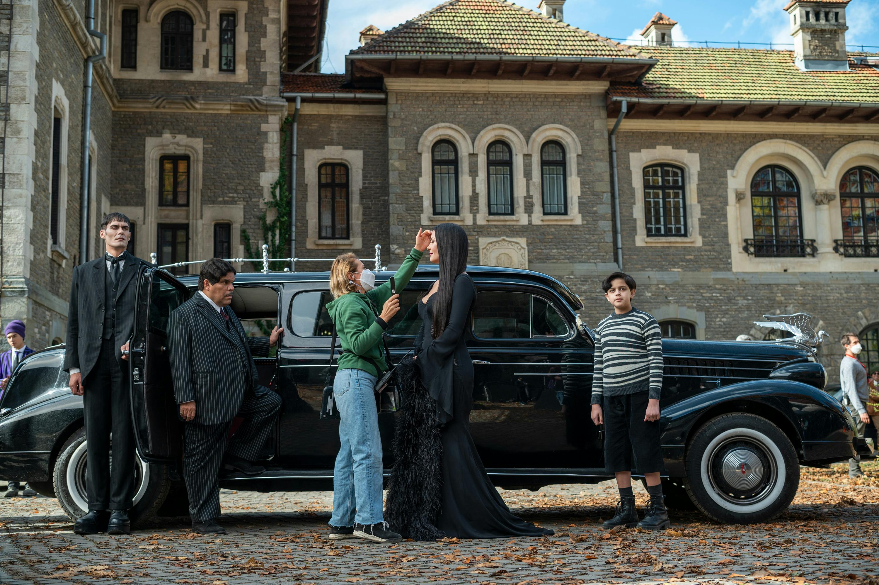Lurch (George Burcea), Gomez Addams (Luis Guzmán), Morticia Addams (Catherine Zeta-Jones), and Pugsley Addams (Issac Ordonez) stand outside a limo at Nevermore Academy.  