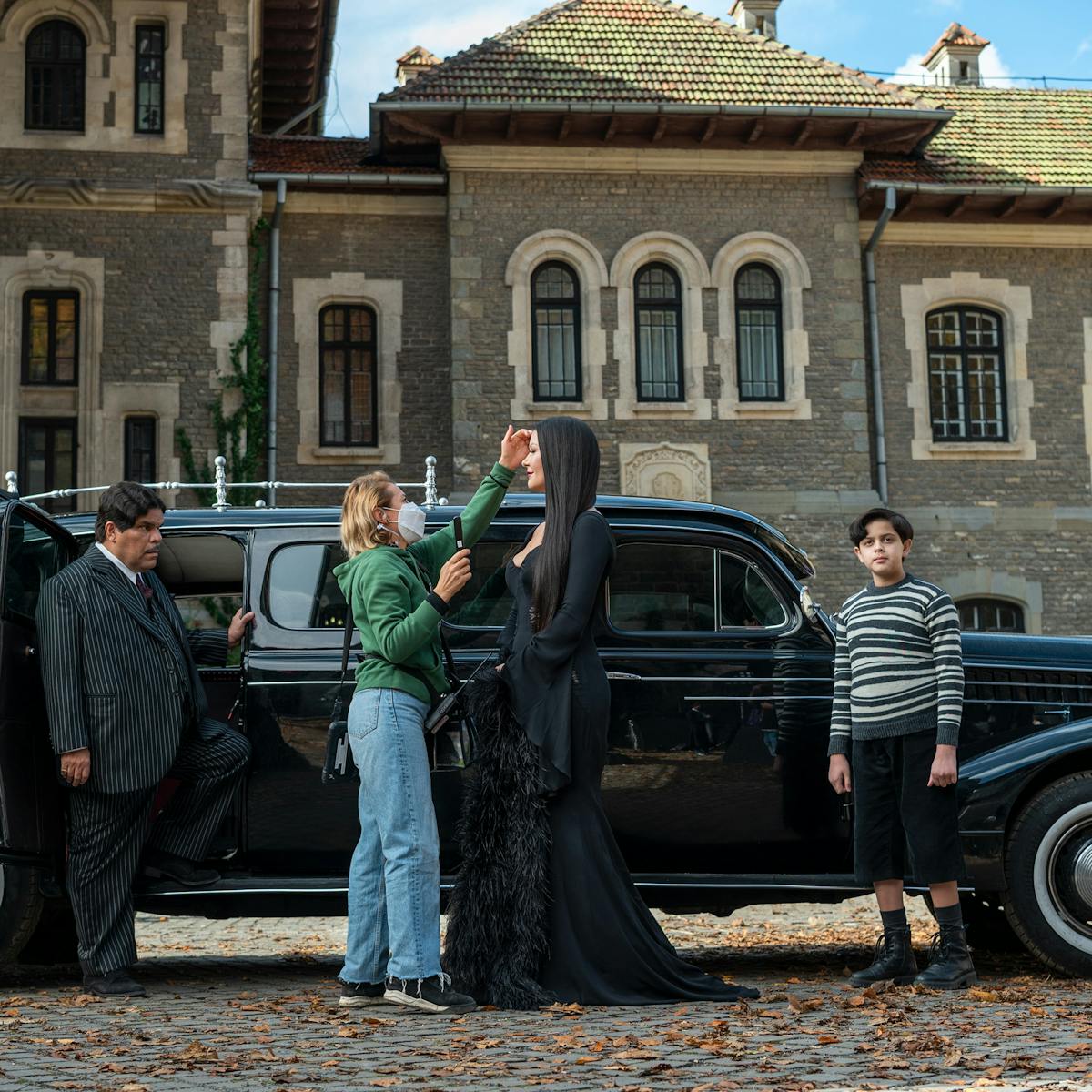 Lurch (George Burcea), Gomez Addams (Luis Guzmán), Morticia Addams (Catherine Zeta-Jones), and Pugsley Addams (Issac Ordonez) stand outside a limo at Nevermore Academy.  