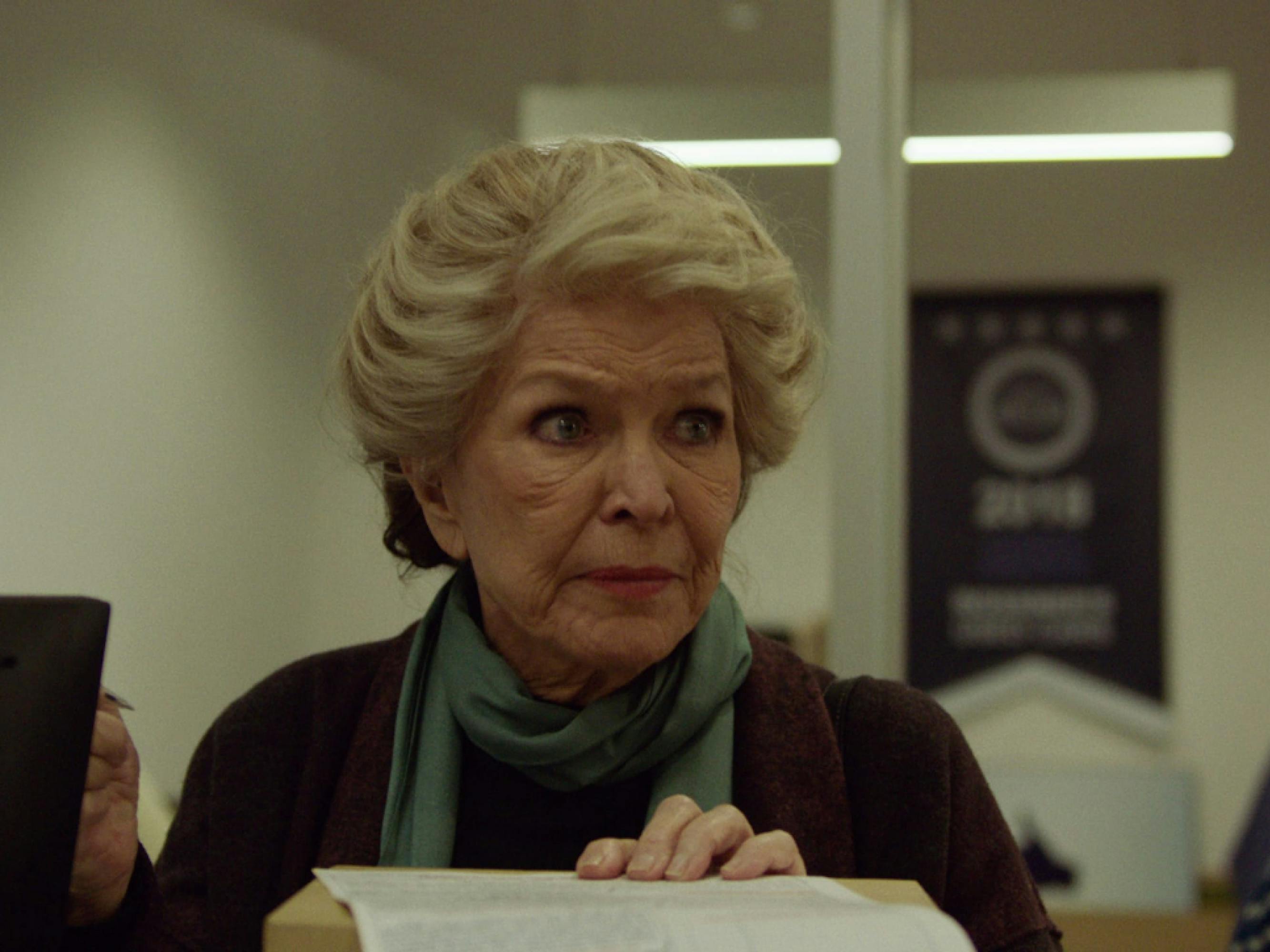Ellen Burstyn as Elizabeth Weiss in a still from Pieces of a Woman. Her large blue eyes match the thin scarf tied around her neck, and her white hair is styled in an elegant up-do.  