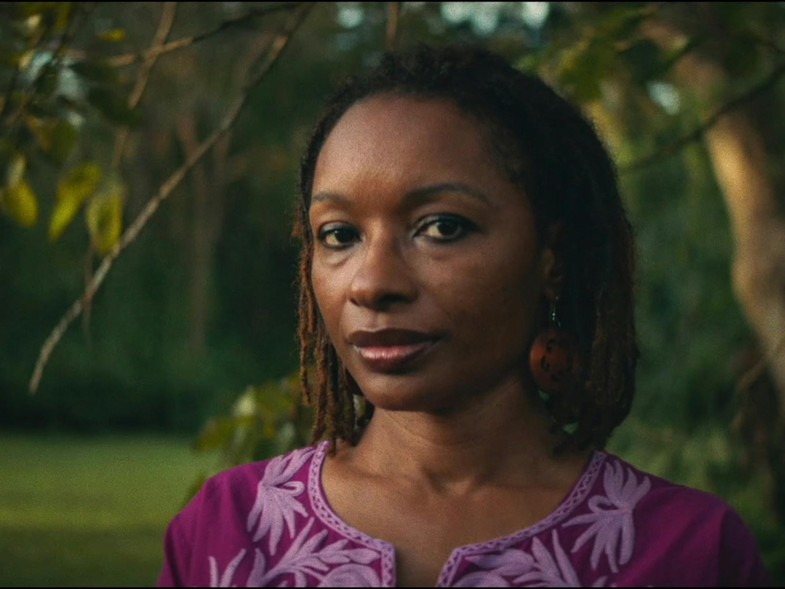 Veda Tunstall wears a pink top and stands in a grassy clearing.