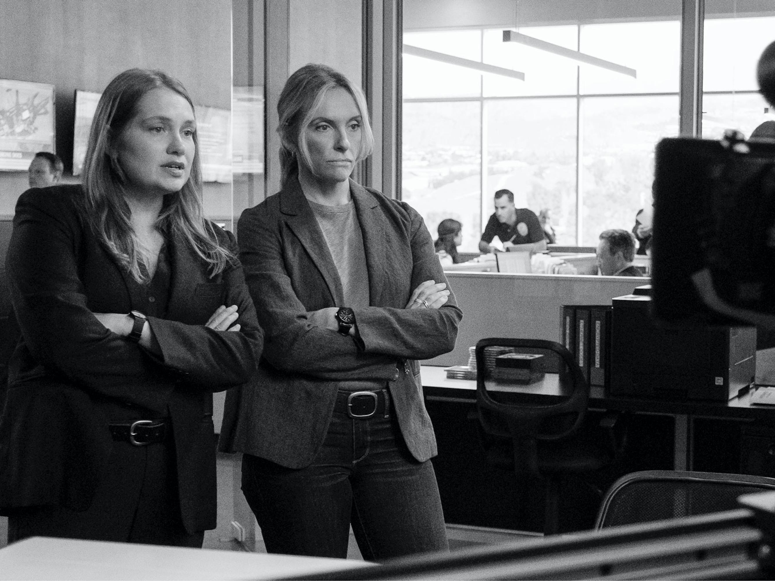 Toni Collette and Merritt Wever wear blazers and cross their arms across their chests.